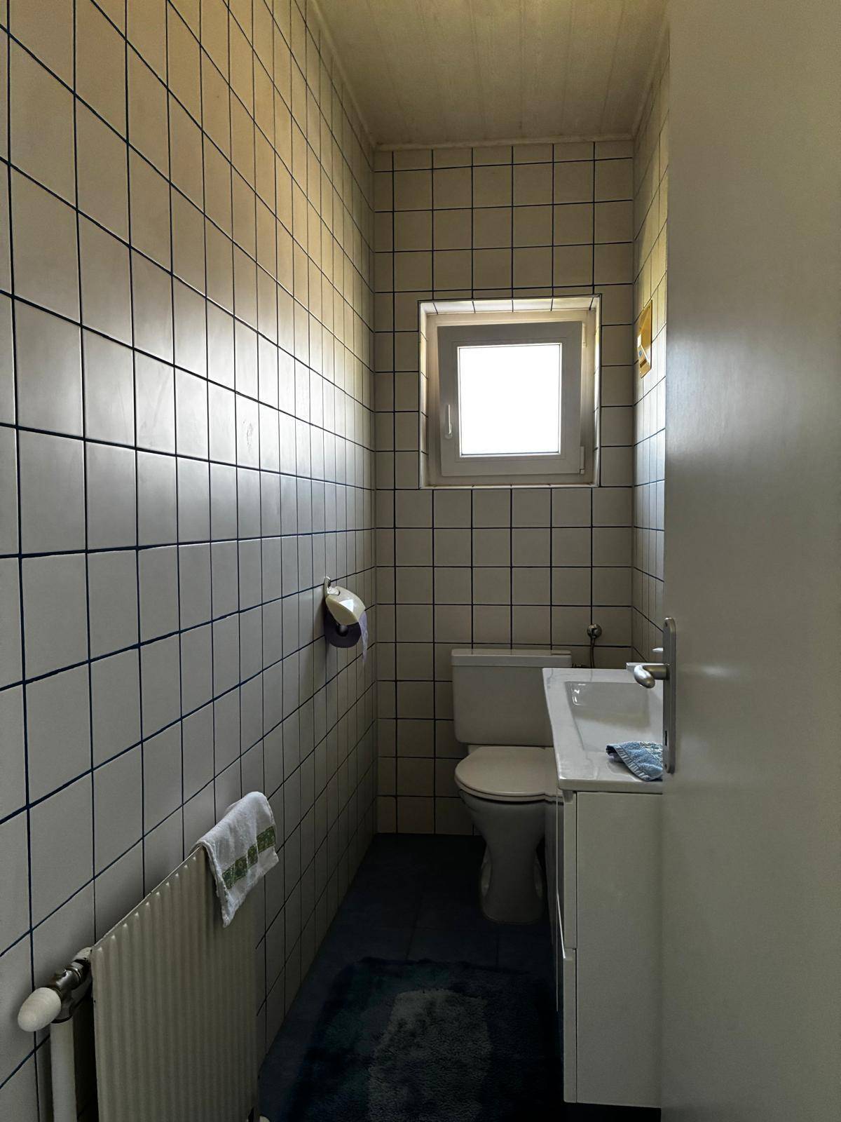 Schlichtes Gäste-WC mit Fenster, weißen Fliesen und einem kleinen Waschbecken.