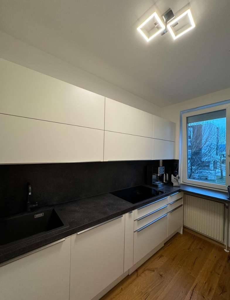 Moderne Küche mit weißen Oberschränken, dunkler Arbeitsplatte und Induktionskochfeld.