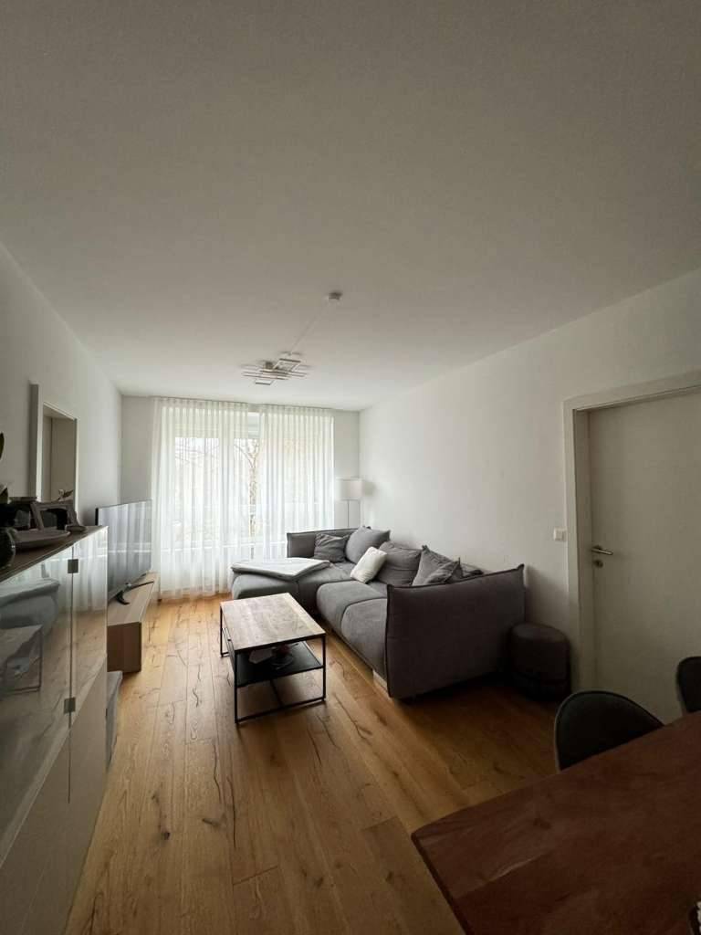 Heller Wohnbereich mit großem Sofa, Holzboden und Zugang zum Essbereich.