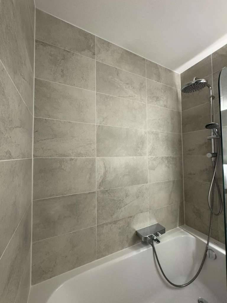 Modern gefliestes Badezimmer mit Badewanne und integrierter Duschfunktion.