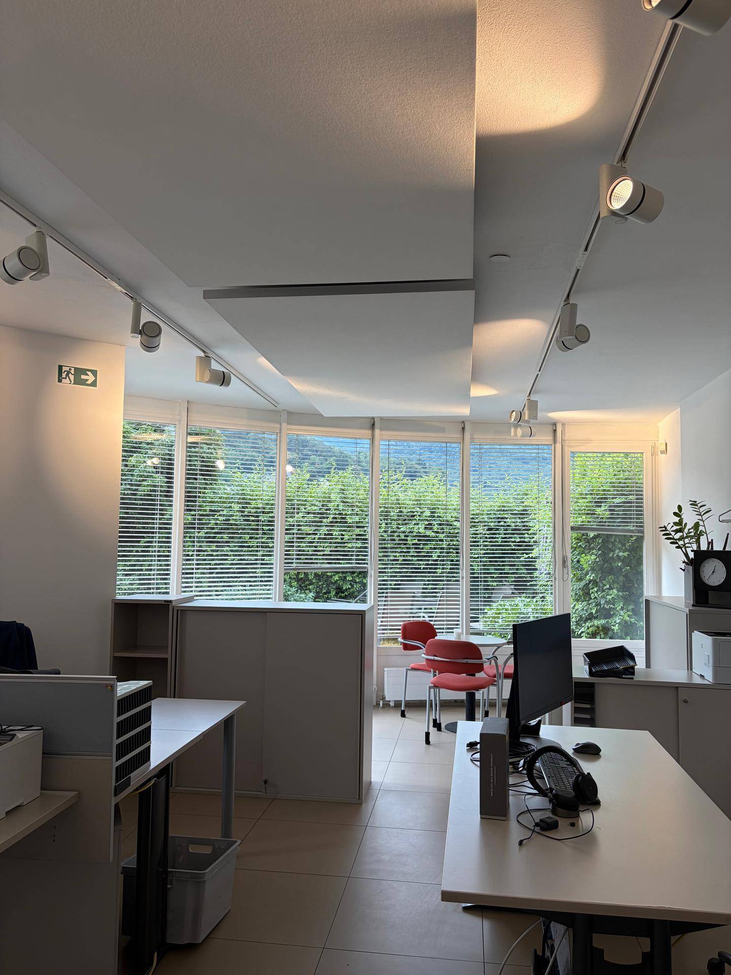 Geräumiges Büro mit mehreren Arbeitsbereichen, Jalousien an den Fenstern und einem kleinen Besprechungsbereich.