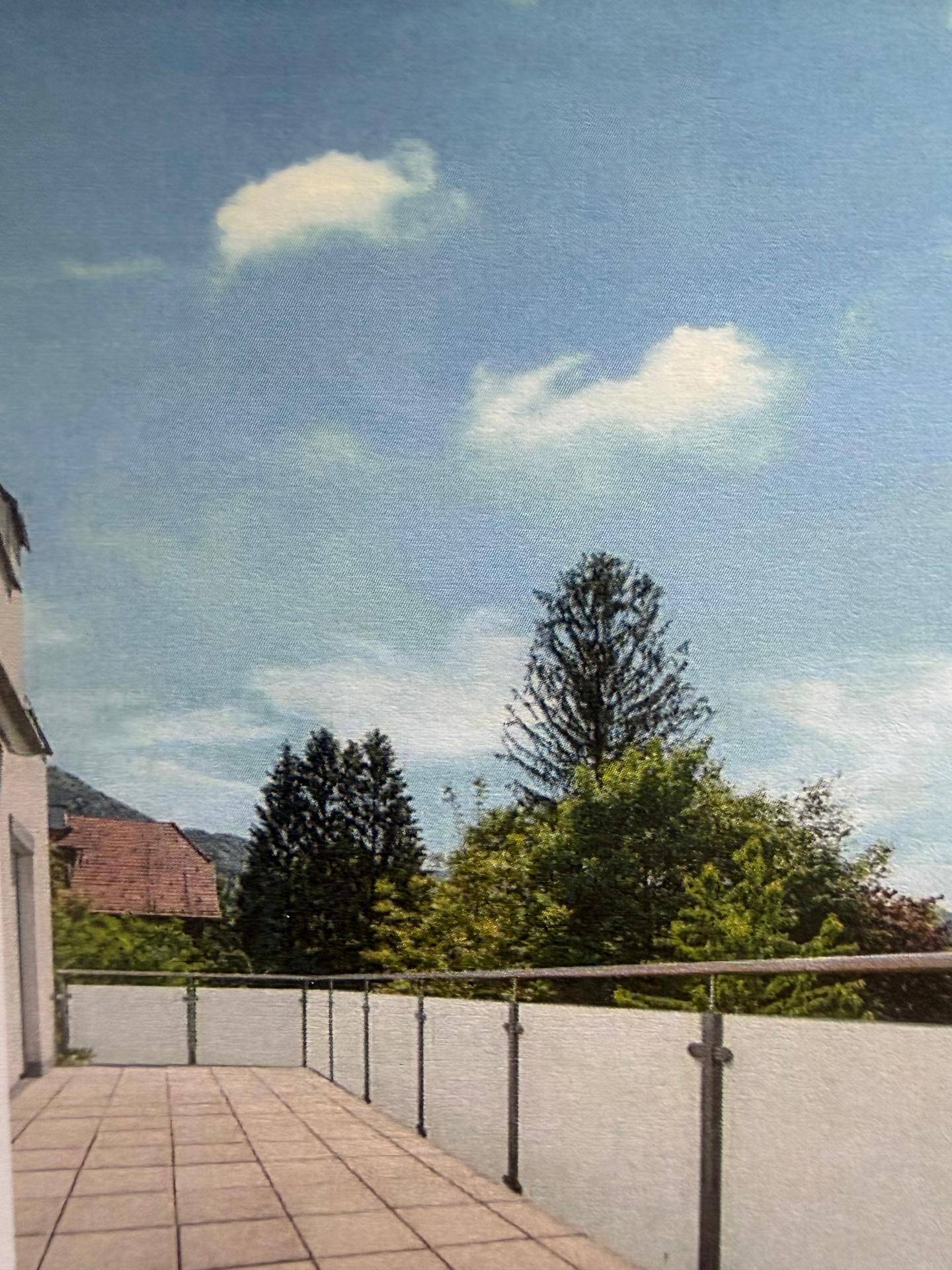 Geräumige Terrasse mit Fliesenboden und Glasgeländer, umgeben von grünen Bäumen.
