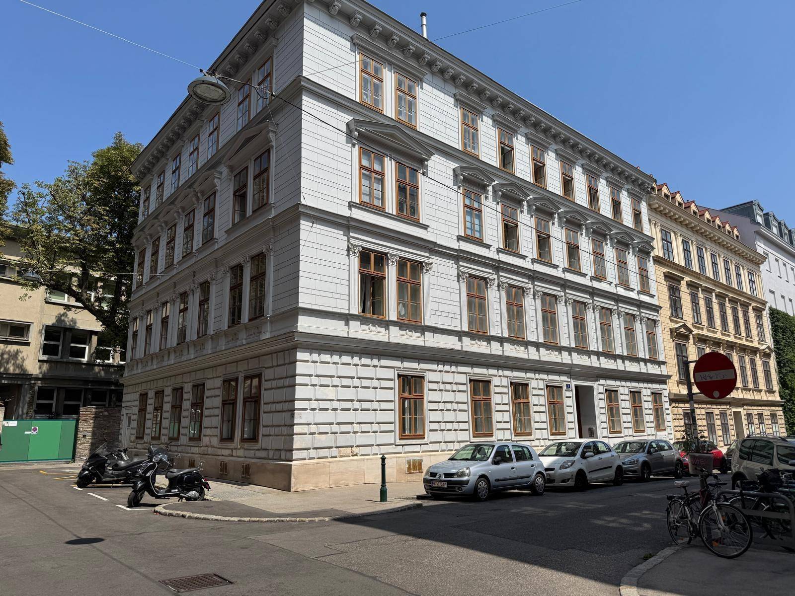 Eckansicht eines historischen Gebäudes mit detaillierter Fassade und parkenden Autos auf der Straße.