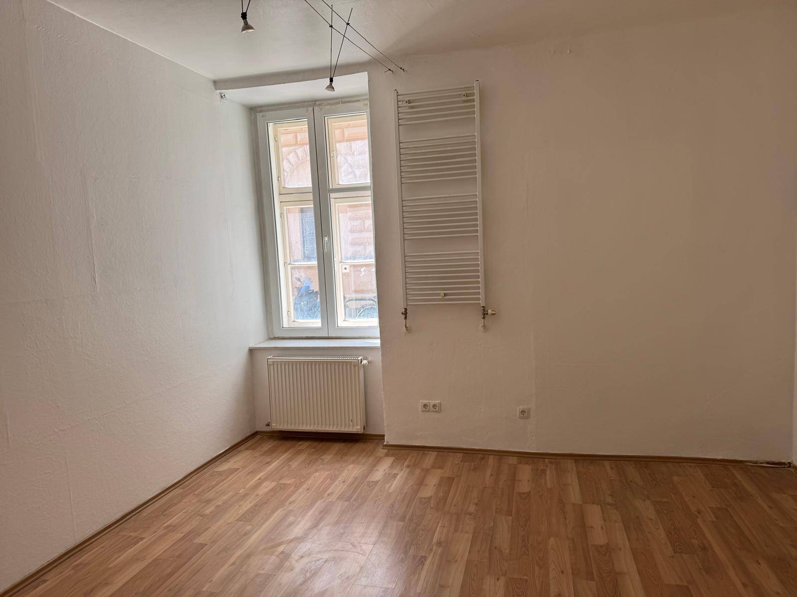 Leerer Raum mit Holzboden, weißen Wänden und einem Fenster, bereit zur individuellen Gestaltung.