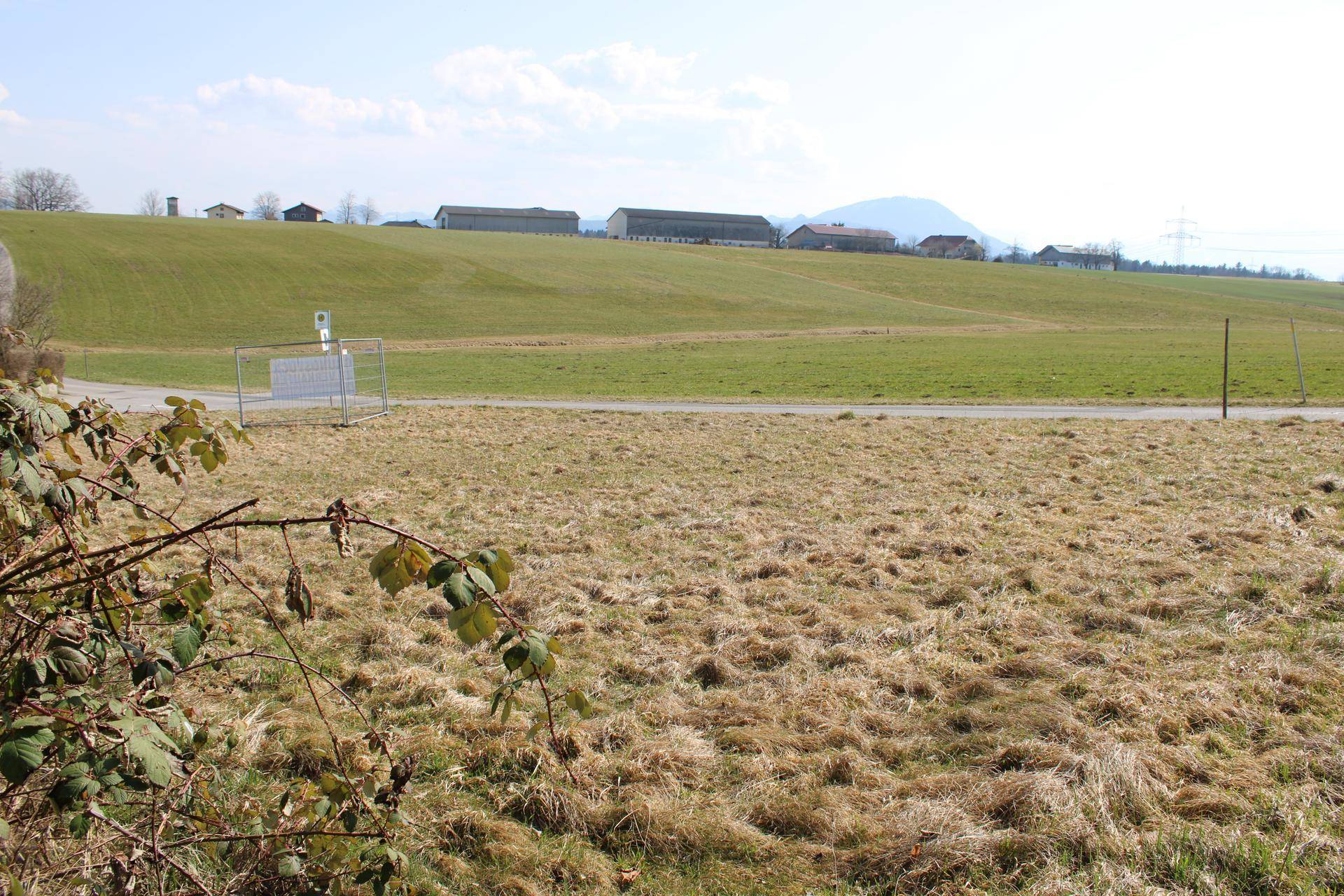 Offenes Feld mit weitem Blick auf die umliegende Landschaft und entfernte Gebäude unter blauem Himmel.