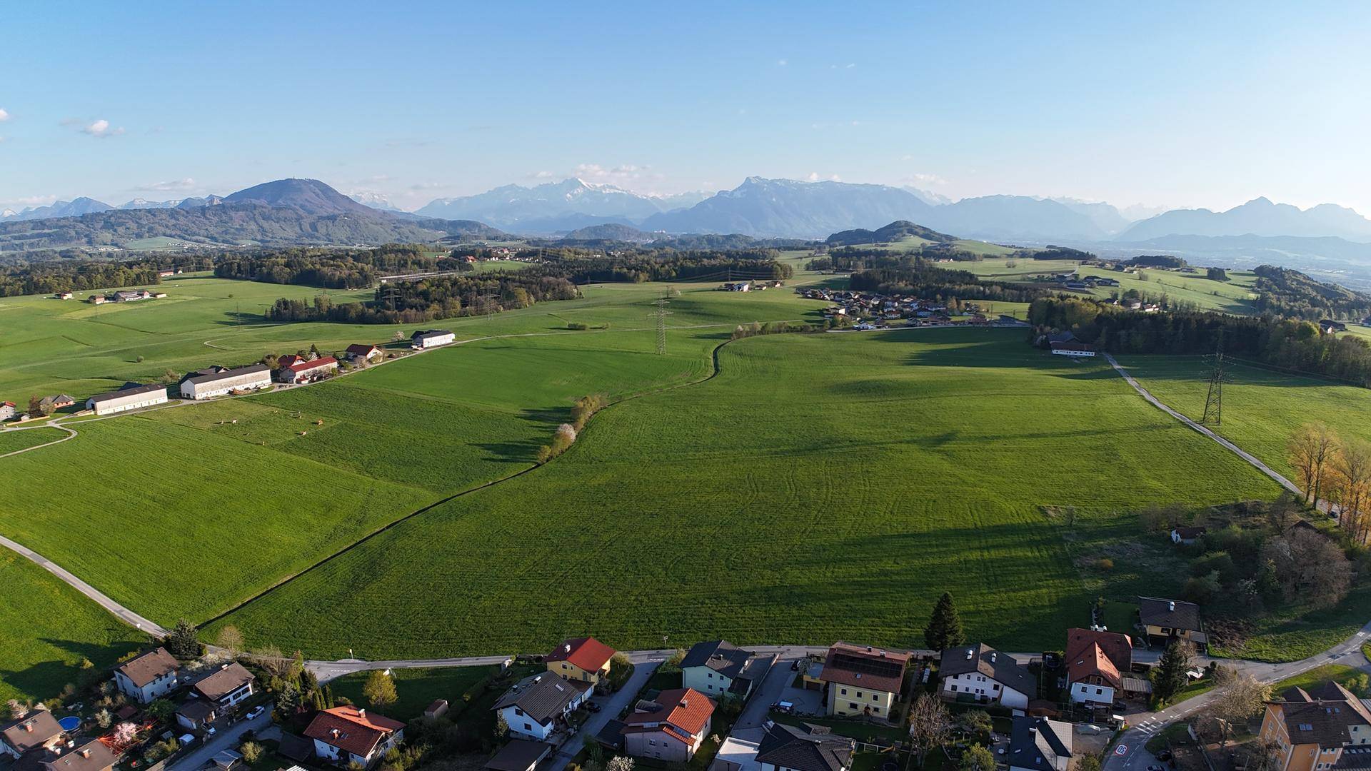 Panoramablick über eine ländliche Siedlung mit grünen Feldern und majestätischen Bergen am Horizont.