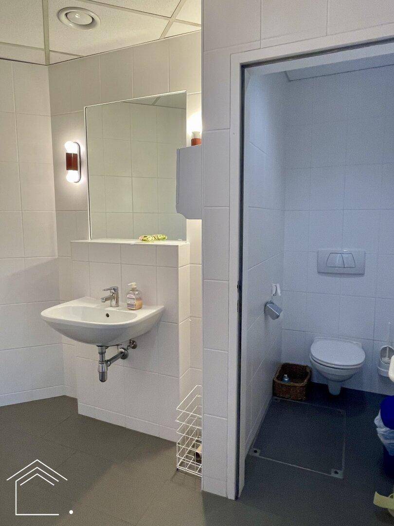 Heller Waschraum mit Waschbecken und separater Toilettenkabine, sauber und funktional.