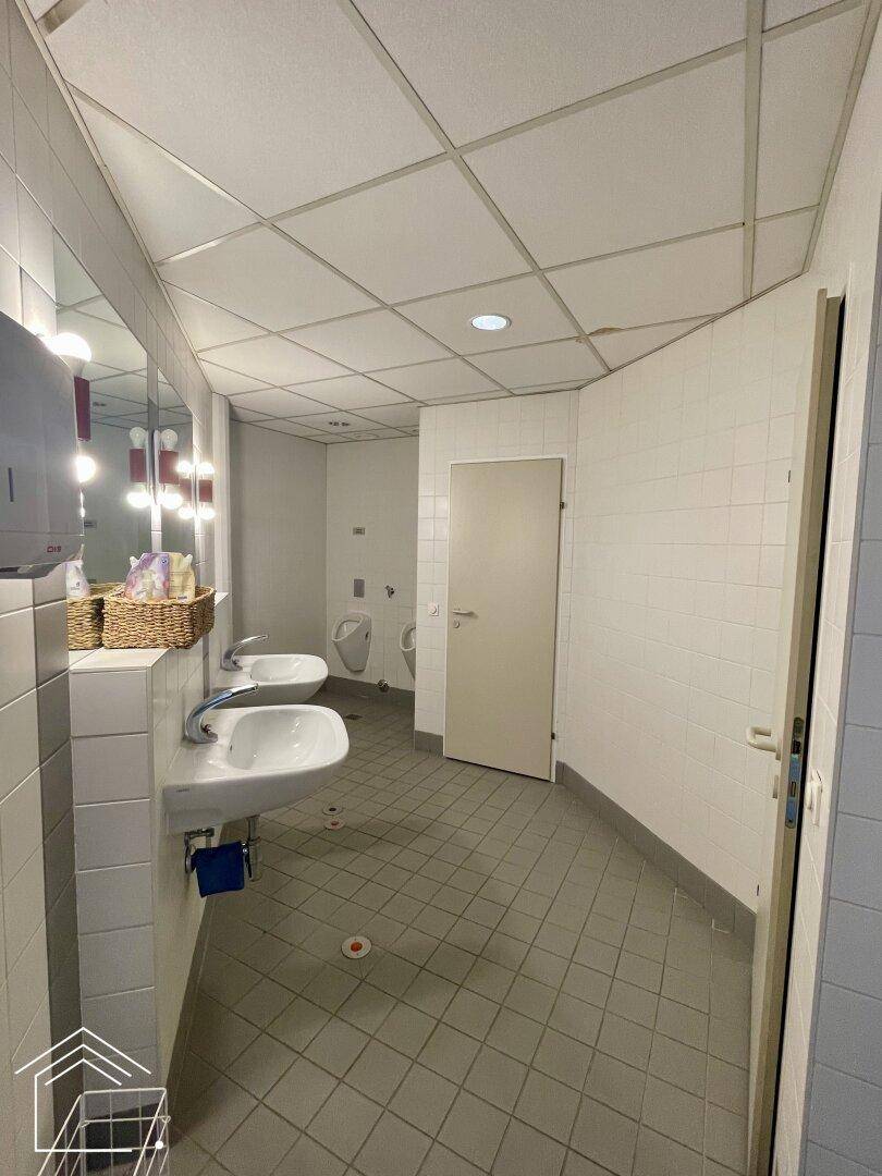 Geräumiger Waschraum mit mehreren Waschbecken und Urinalen, funktional und hell.