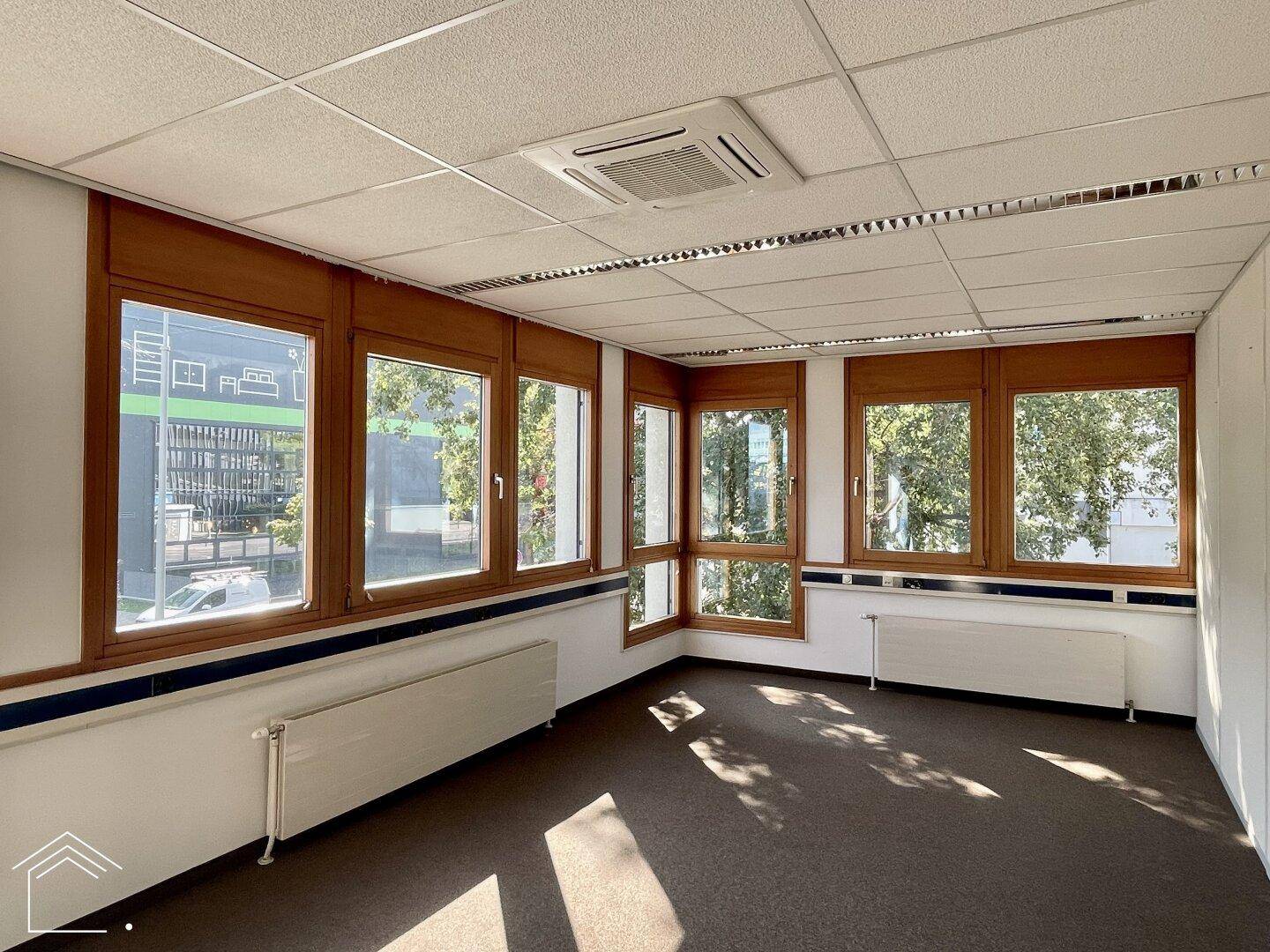 Eckbüro mit Teppichboden, vielen Fenstern und Heizkörpern, bietet viel Tageslicht und Ausblick.