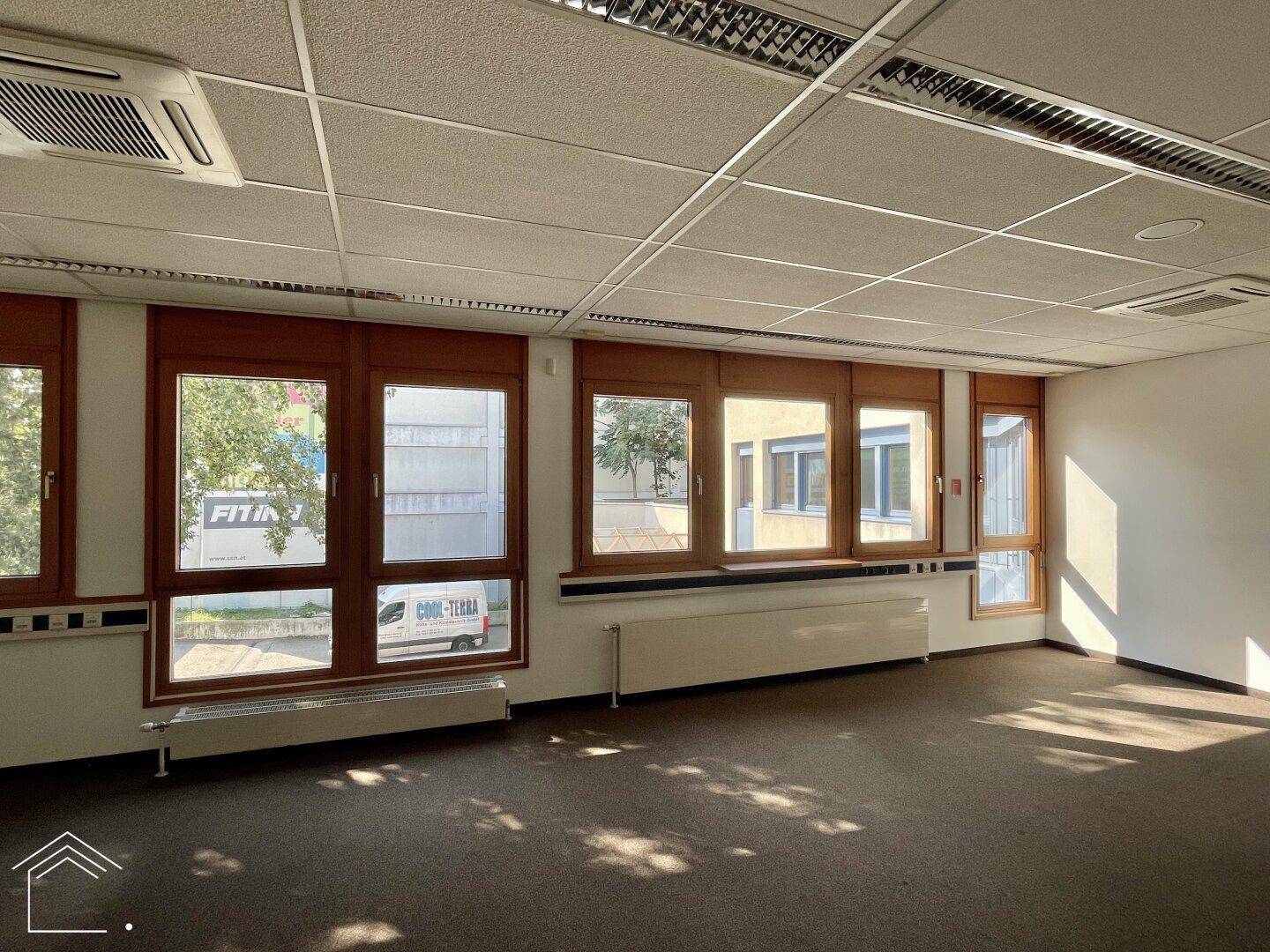Büro mit Teppichboden, großen Fenstern und Blick auf die Straße, ausgestattet mit Klimaanlage.
