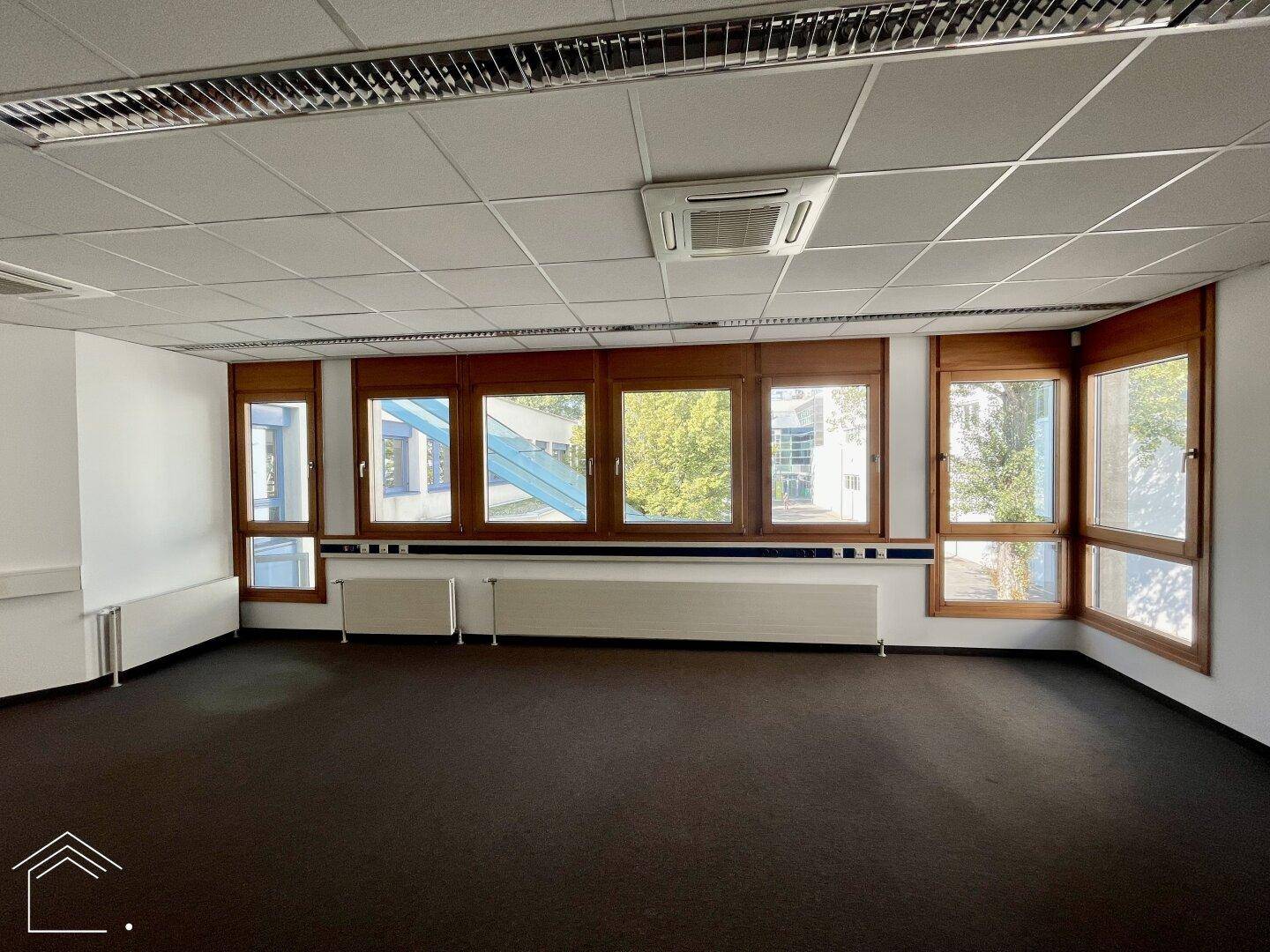 Helles Büro mit Teppichboden, breiten Fenstern und Klimaanlage, bietet eine angenehme Arbeitsumgebung.