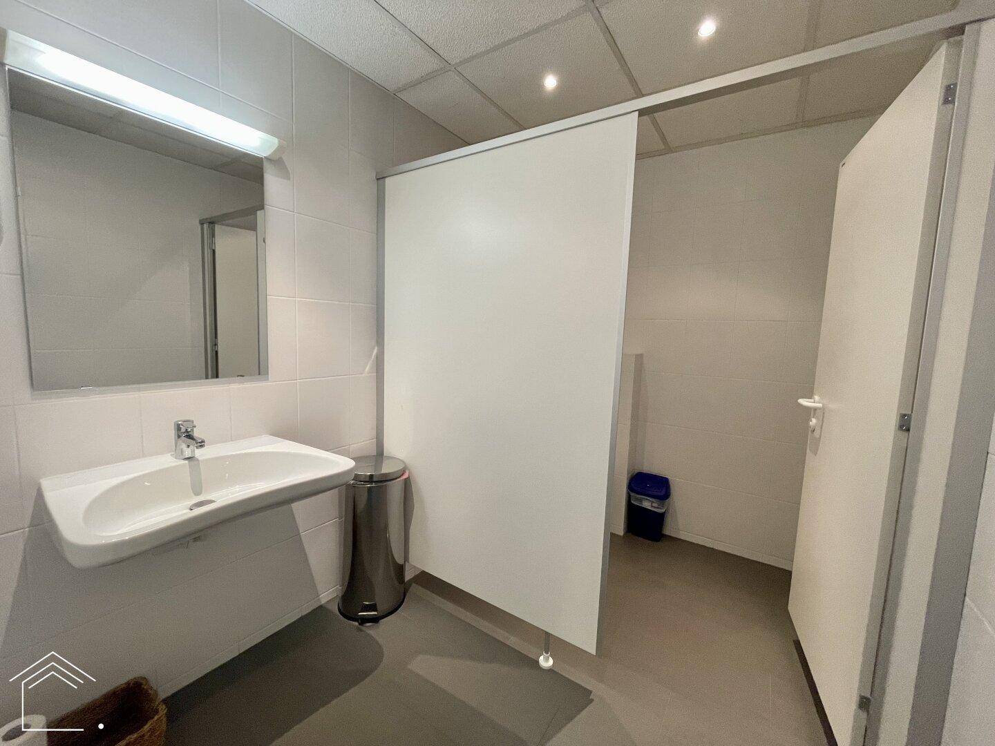 Sauberer Waschraum mit Waschbecken, Spiegel und Toilettenkabinen, funktional und gut gepflegt.