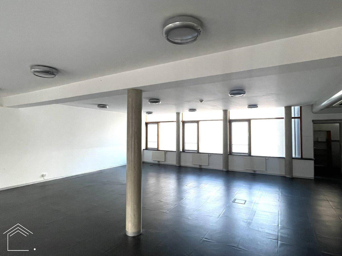 Weitläufiger Bürobereich mit großen Fenstern, dunklem Boden und einer tragenden Betonsäule, die den Raum gliedert.
