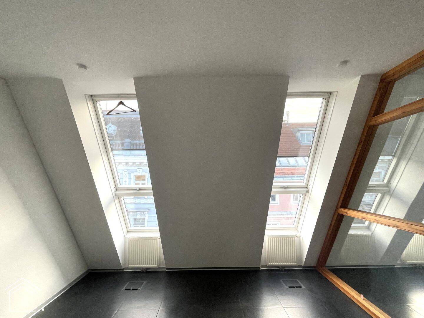 Zwei schräge Dachfenster mit Heizkörpern darunter, die viel Tageslicht in den Raum lassen.