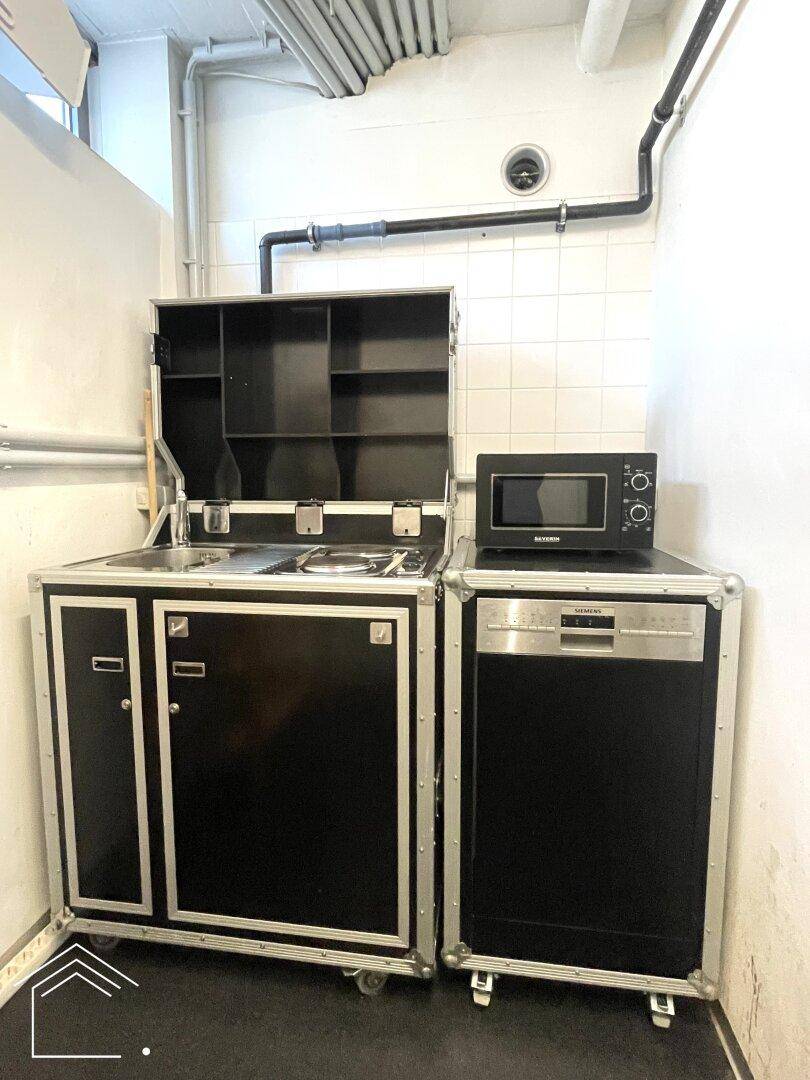Kleine, funktionale Küchenzeile mit mobilen Schränken, Spüle, Kochfeld, Mikrowelle und Geschirrspüler.
