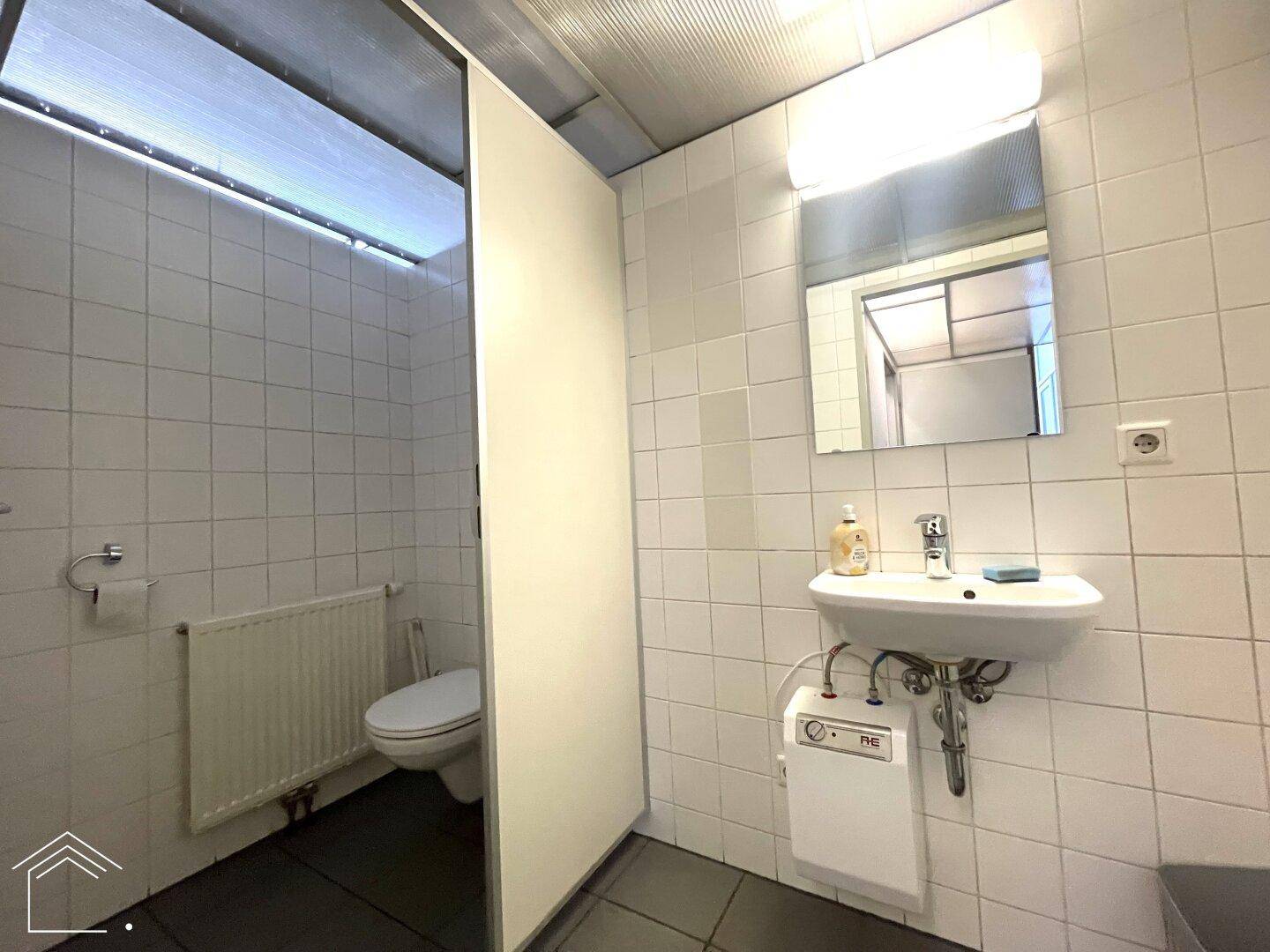 Einfache Toilette mit weißen Fliesen, Waschbecken und Heizkörper, in einem funktionalen Stil.