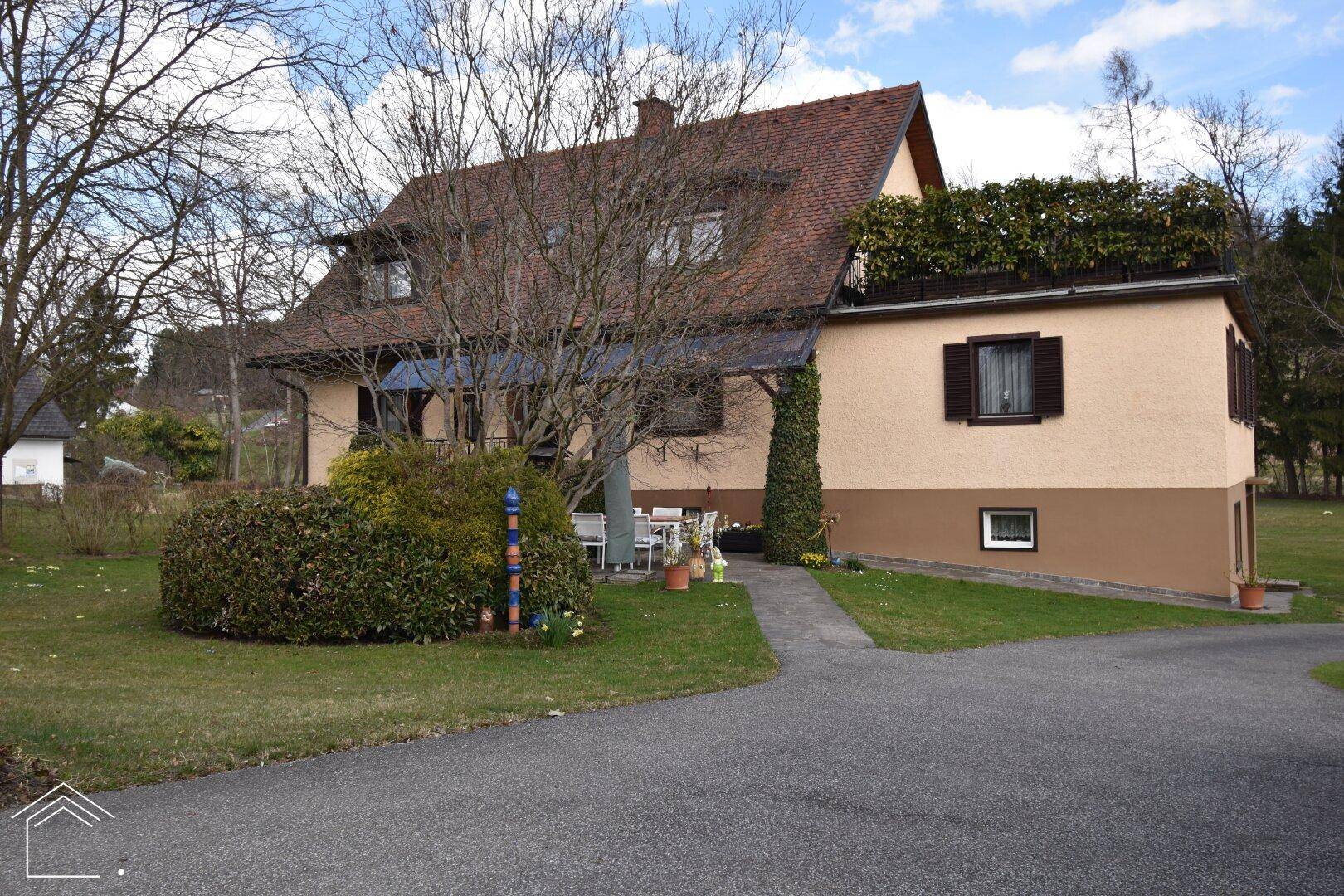 Das Haus von der Seite mit Zufahrt, Rasenfläche und Blick auf die grüne Umgebung.