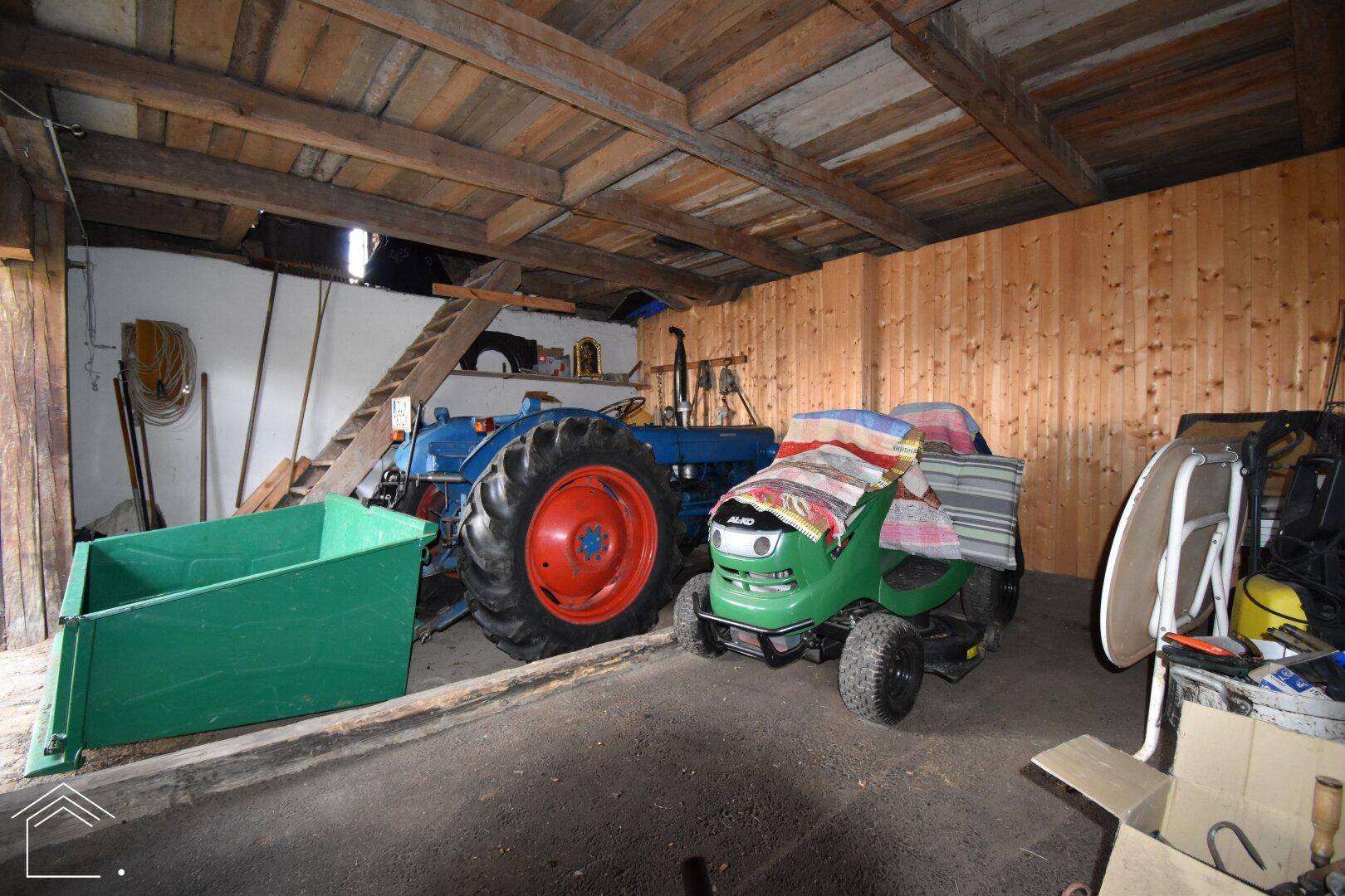 Innenraum der Garage mit landwirtschaftlichen Geräten und einer Holzdecke.
