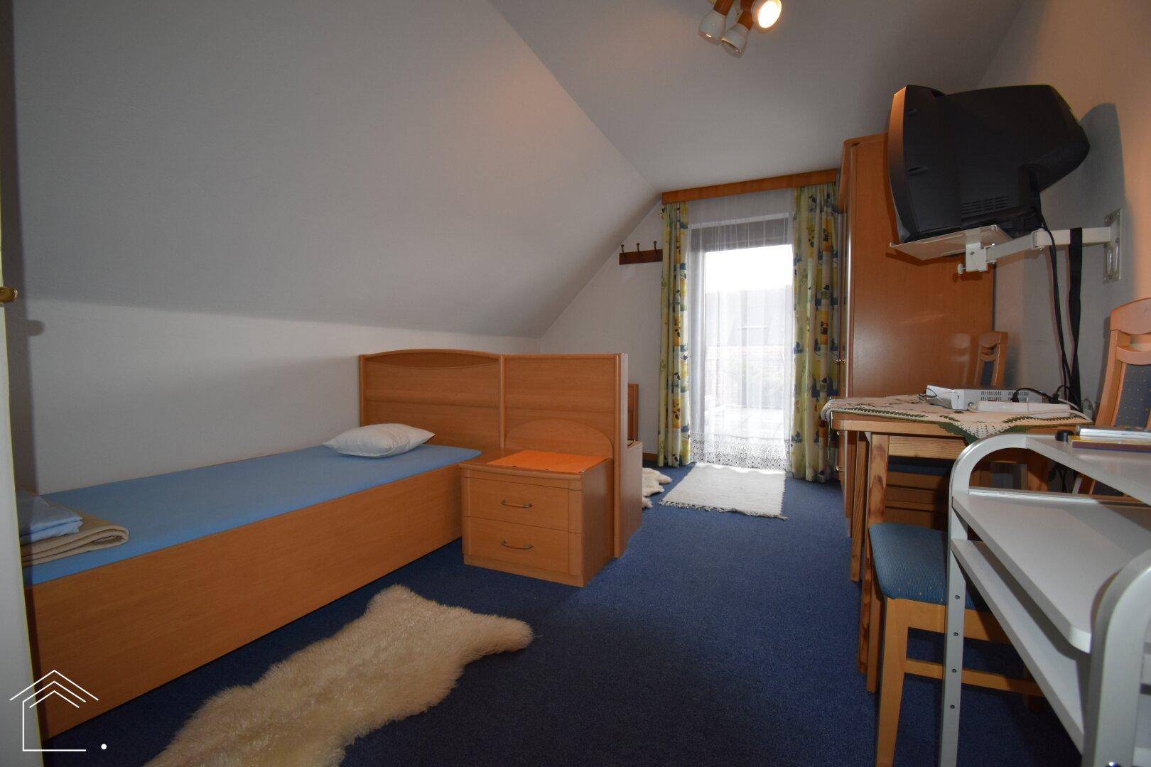 Schlafzimmer mit Einzelbett, Schreibtisch und Dachschräge, ideal als Gäste- oder Arbeitszimmer.