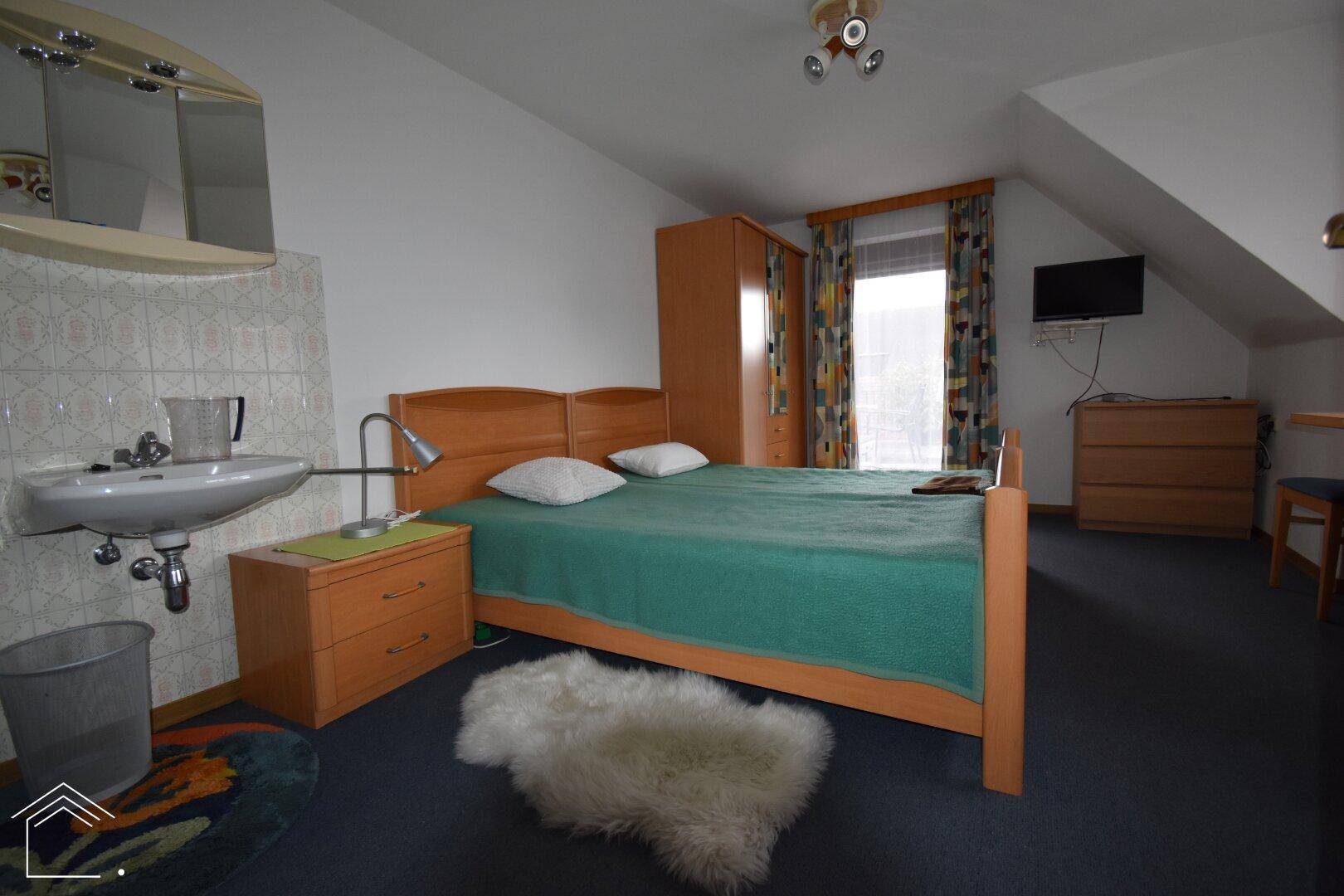Schlafzimmer mit zwei Einzelbetten, einem Waschbecken und Dachschräge, die dem Raum Charakter verleiht.