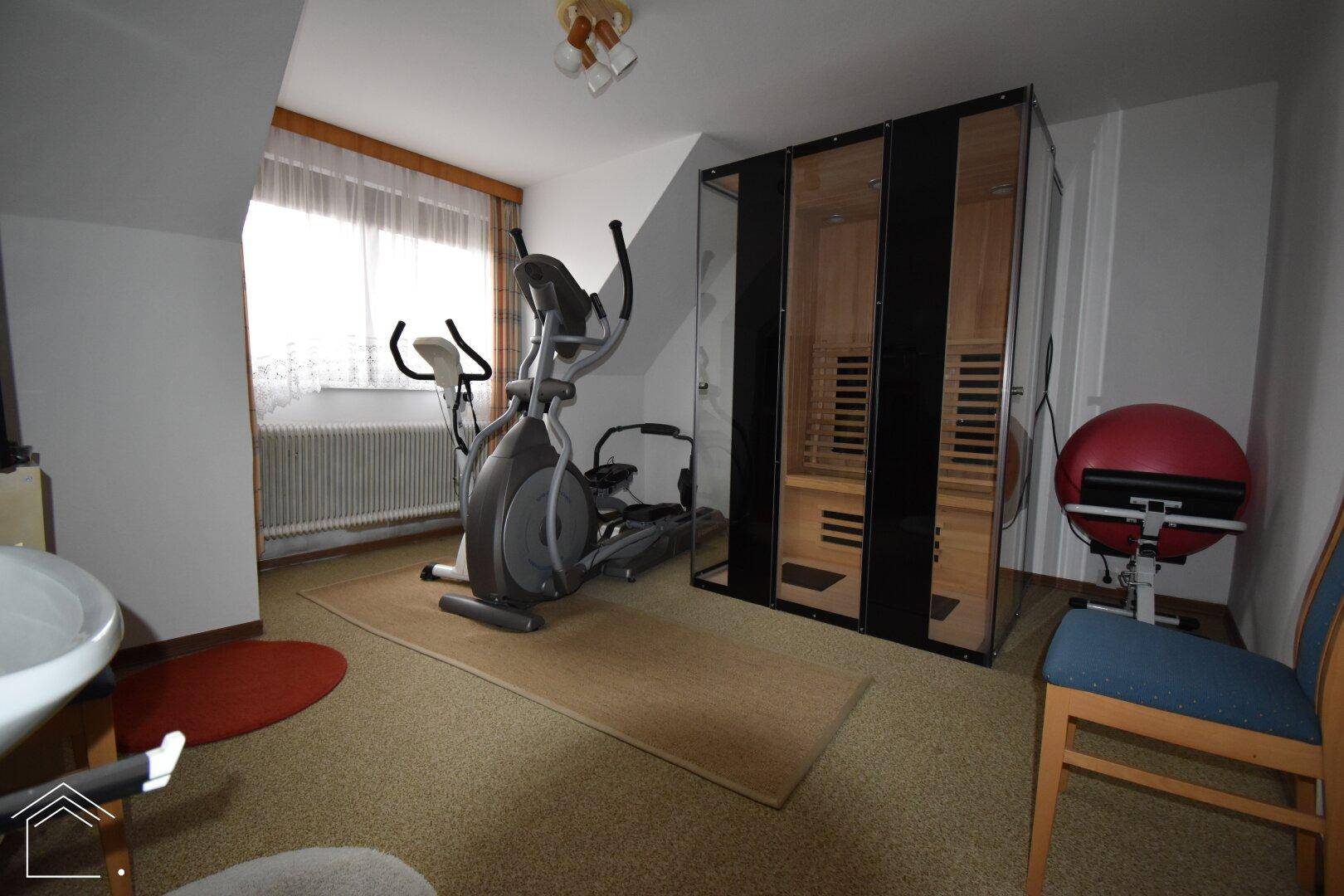 Fitnessraum mit Trainingsgeräten und einer Infrarotkabine unter der Dachschräge.