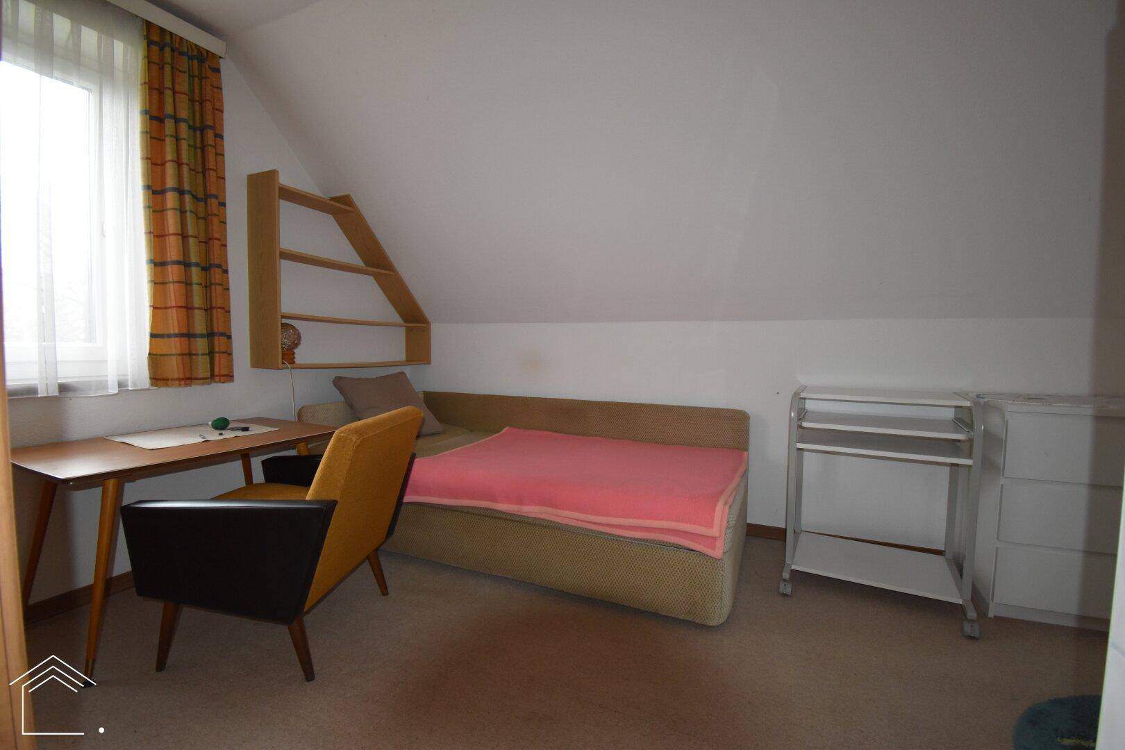 Zimmer mit Einzelbett, Schreibtisch und Regal unter der Dachschräge, vielseitig nutzbar.