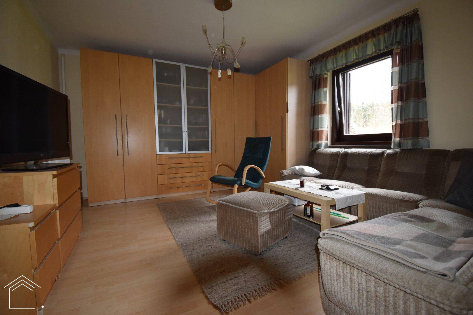 Wohnzimmer mit Sofa, großem Kleiderschrank und Fenster, das den Raum mit Licht erfüllt.