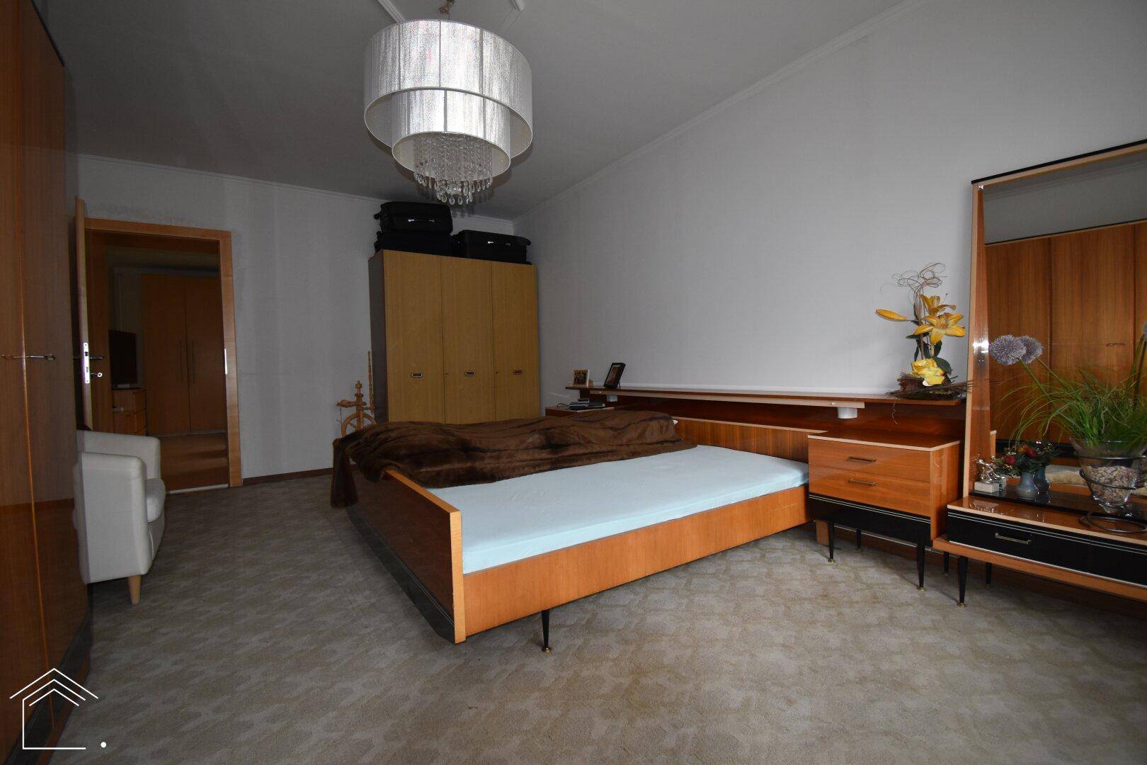 Geräumiges Schlafzimmer mit Doppelbett, klassischer Holzmöblierung und Teppichboden.