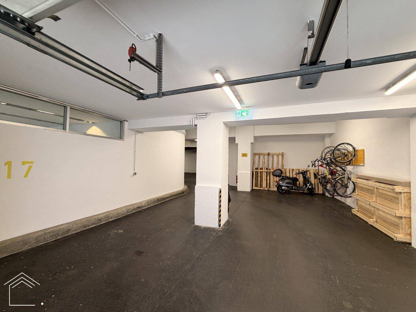 Bereich einer Tiefgarage mit Stellplatz Nummer 17, Lagerflächen und Fahrrädern an der Wand.