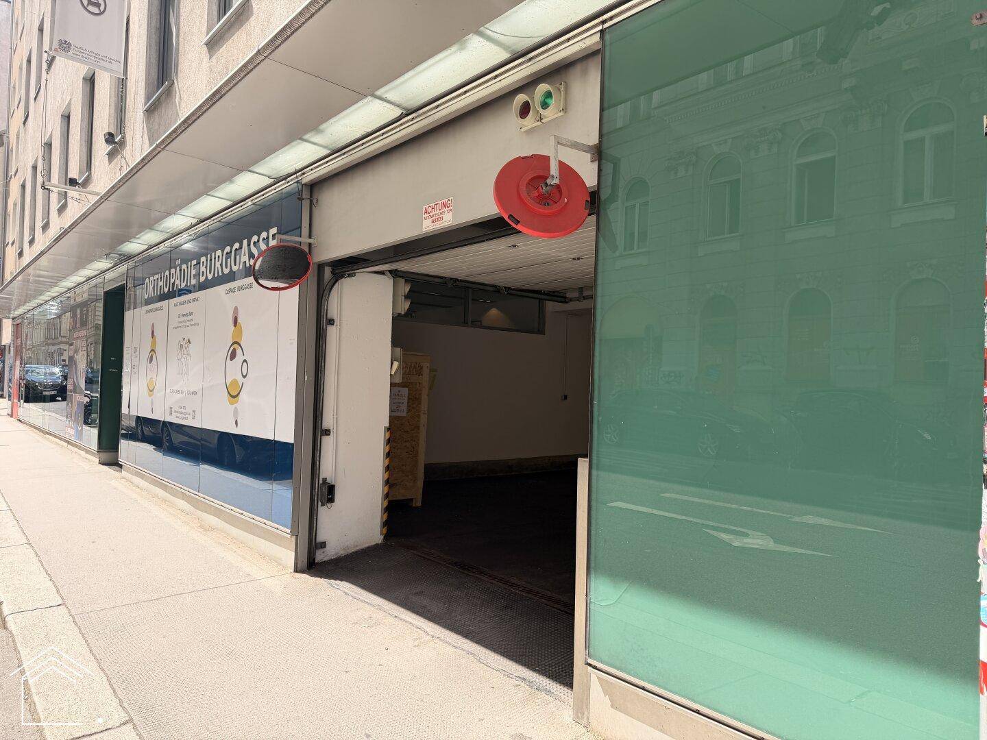 Eingang zur Tiefgarage von der Straße aus gesehen, neben einem Geschäft mit grüner Glasfassade.