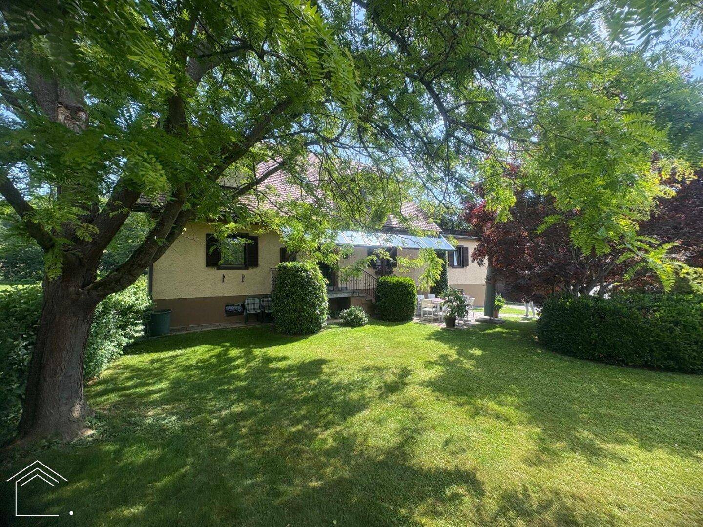 Rückseite des Hauses mit Terrasse, Gartenmöbeln und üppiger grüner Bepflanzung.