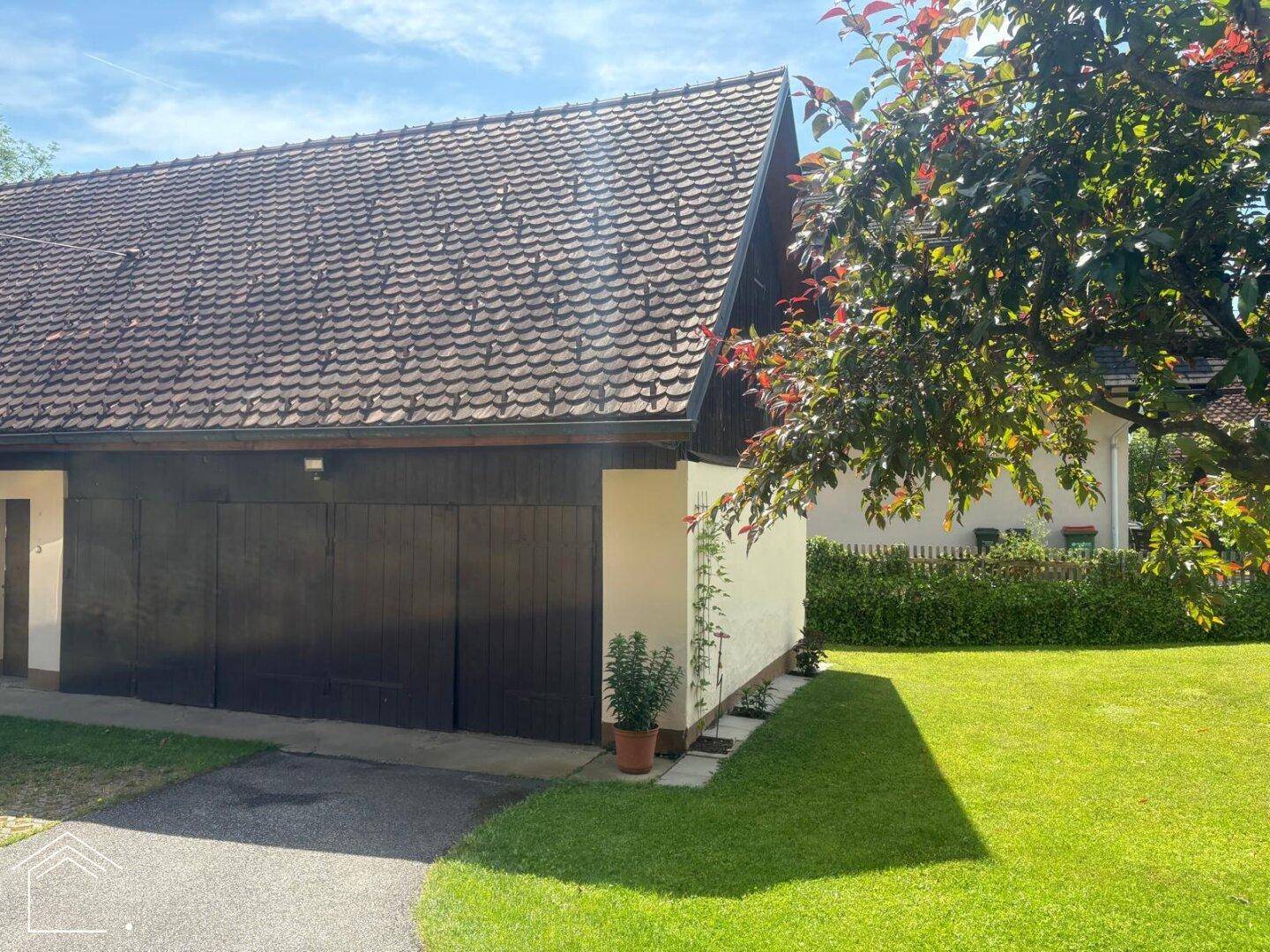 Seitliche Ansicht der Garage mit dunklen Holztoren und gepflegtem Rasen.