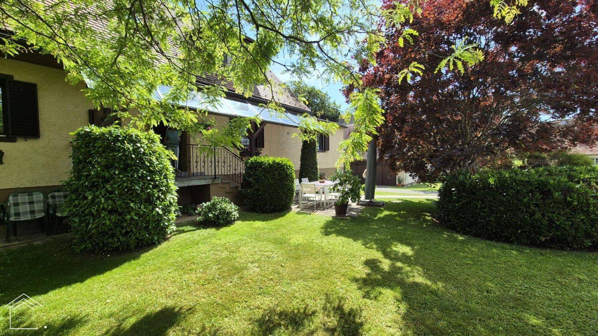 Haus mit gepflegtem Garten, Rasenfläche und einer kleinen Sitzgruppe im Freien.