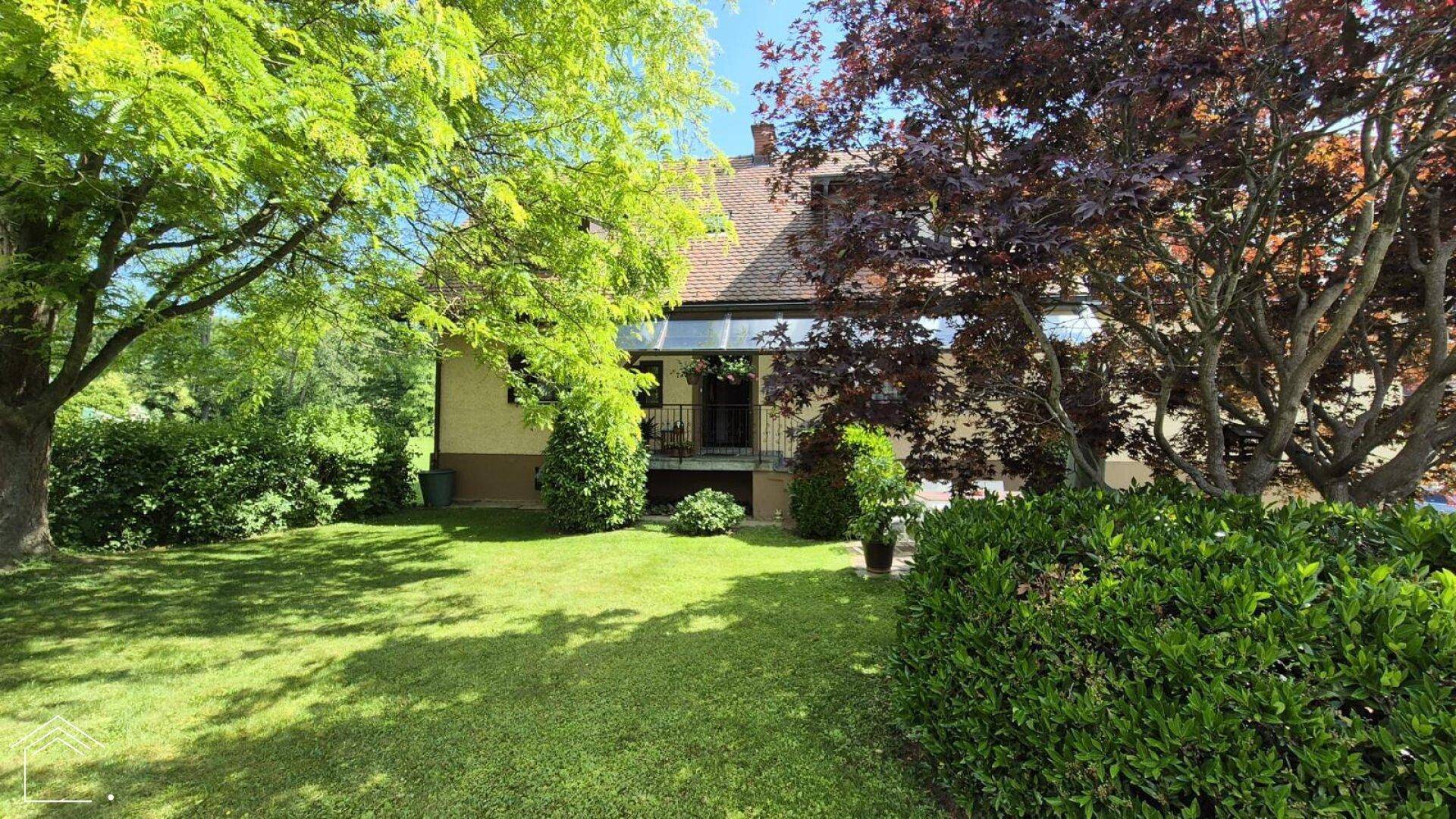 Rückansicht des Hauses mit großem Garten, üppigen Bäumen und grüner Hecke.