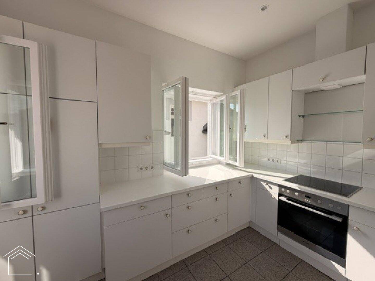 Moderne weiße Küche mit integrierten Geräten, Fliesenboden und geöffnetem Fenster.
