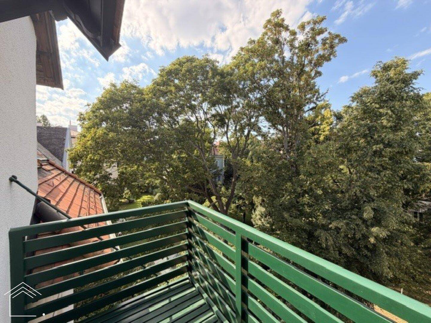 Grüner Balkon mit Blick auf alte Bäume und den blauen Himmel.