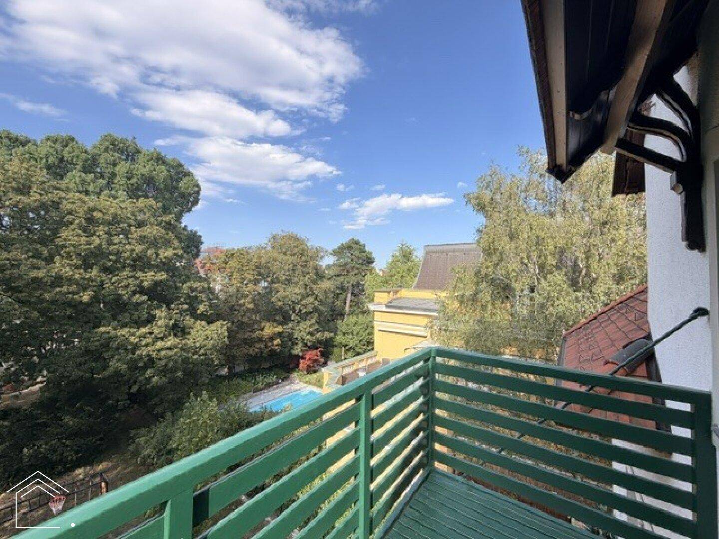 Balkon mit grünen Geländern und weitem Blick über Bäume bis zu einem Pool.