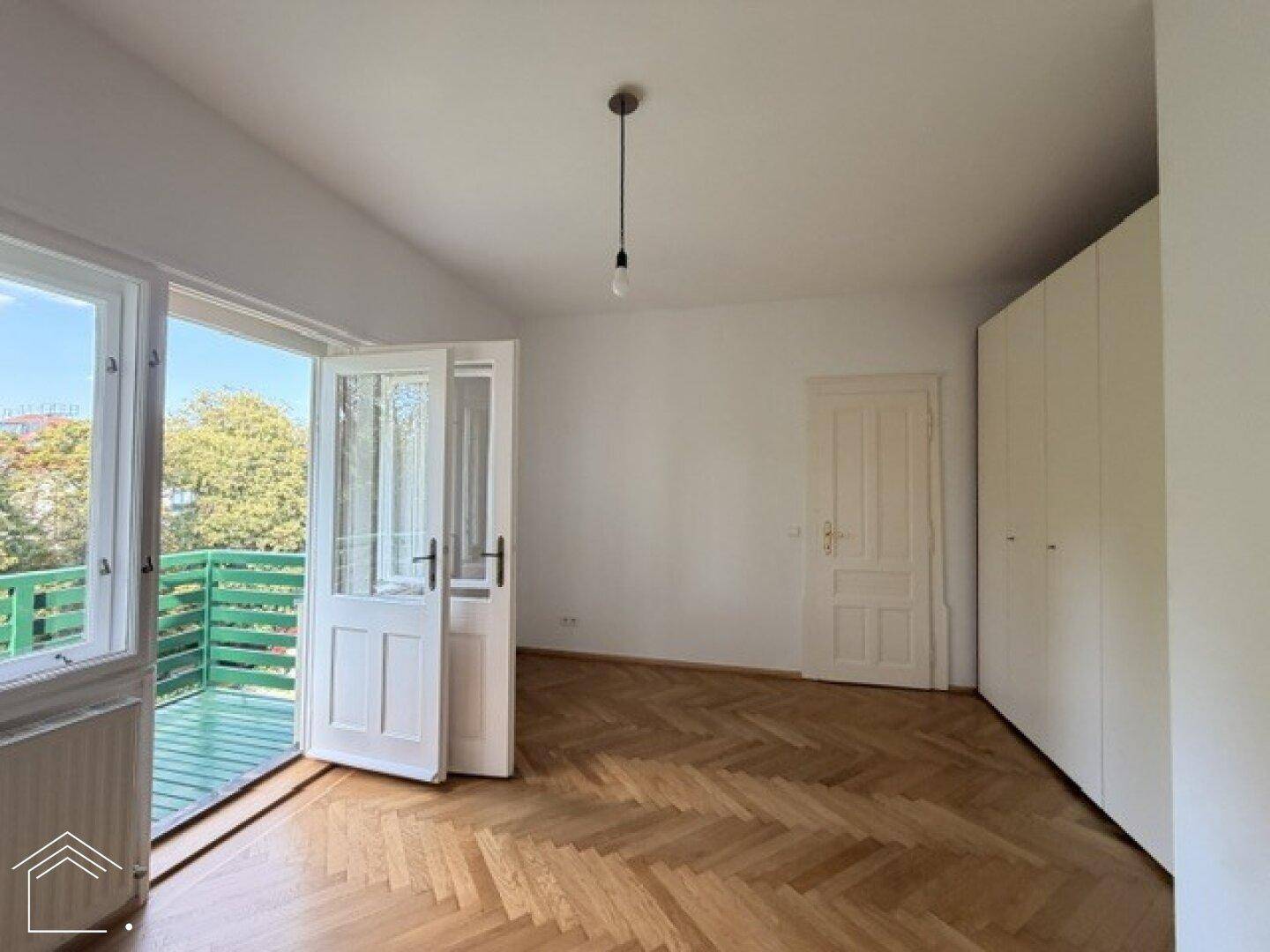 Schlafzimmer mit Fischgrätparkett, Einbauschränken und direktem Zugang zu einem grünen Balkon.