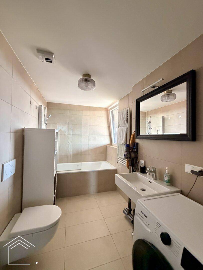 Modernes Badezimmer mit Badewanne, WC, Waschbecken und Waschmaschine, in hellen Fliesen gehalten.