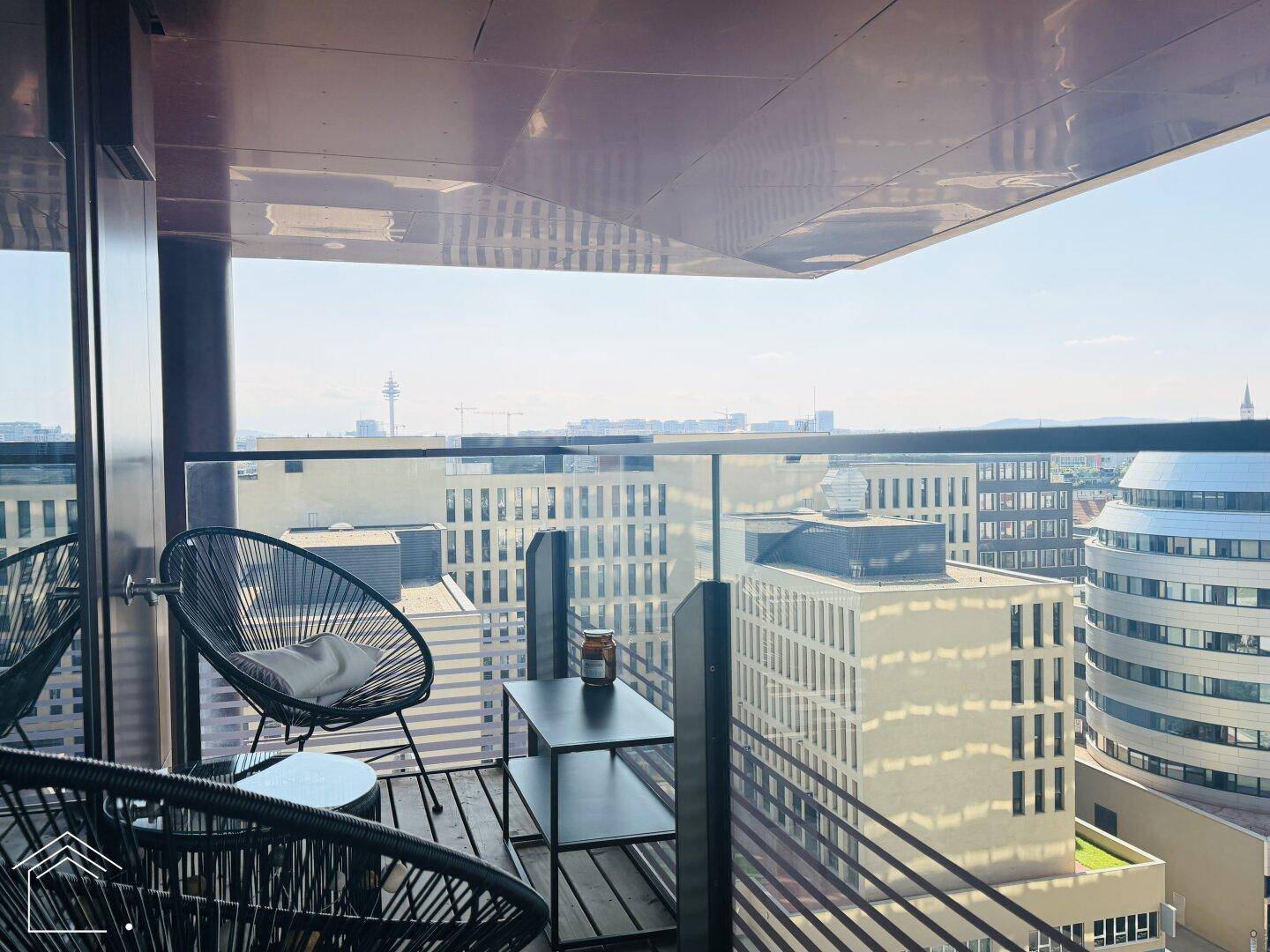 Balkon mit Sitzgelegenheiten und Blick auf moderne Gebäude in der städtischen Umgebung.