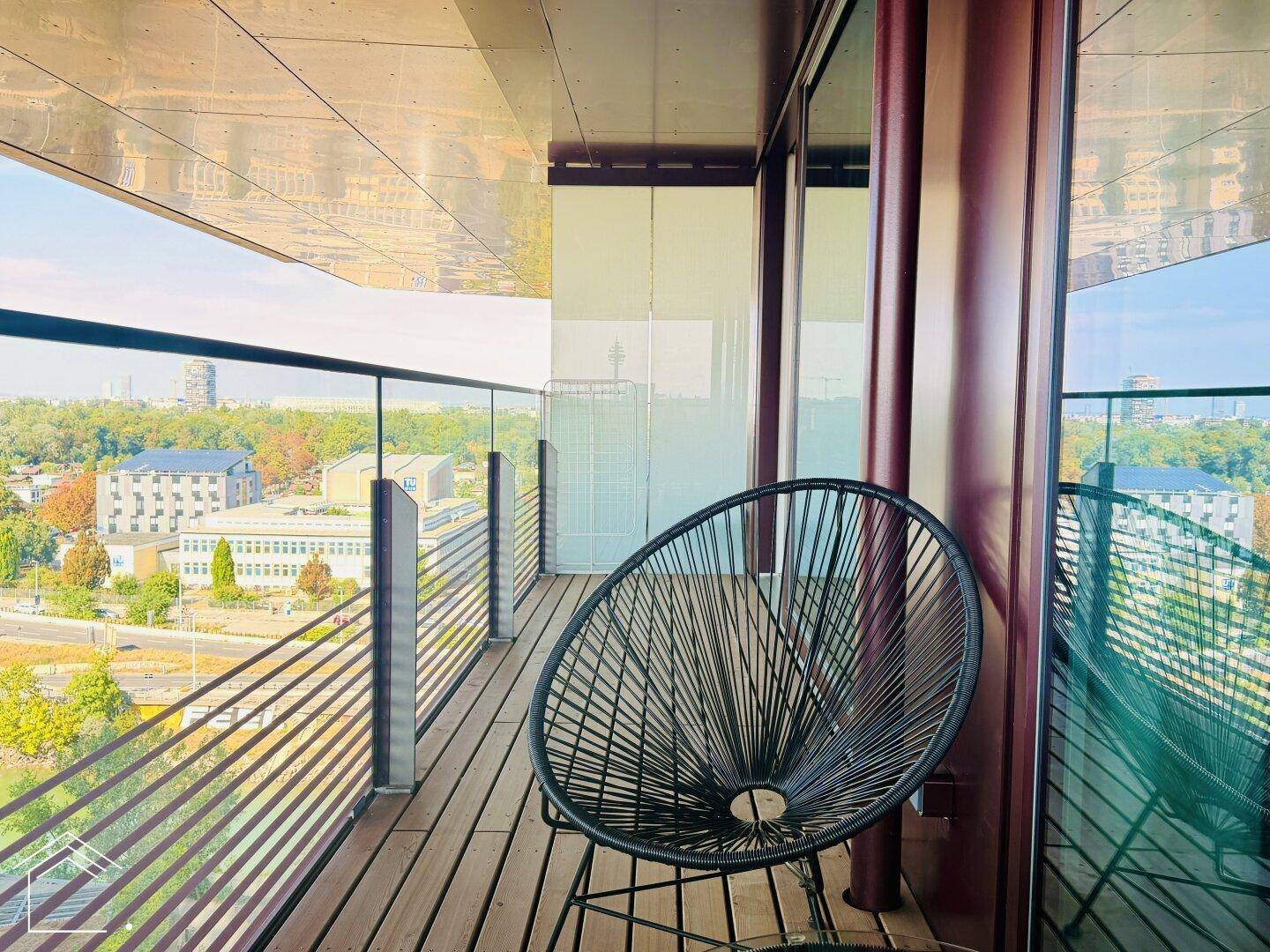 Schmaler Balkon mit einem Stuhl und weitem Blick über die Umgebung und andere Gebäude.