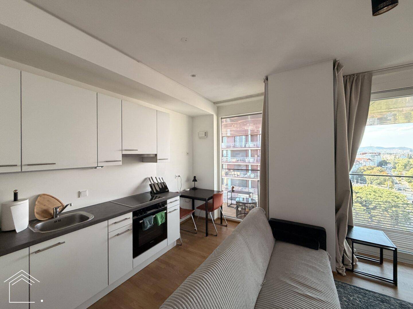 Moderne Küchenzeile mit weißen Schränken, integriertem Essbereich und Sofa in hellem Wohnraum.
