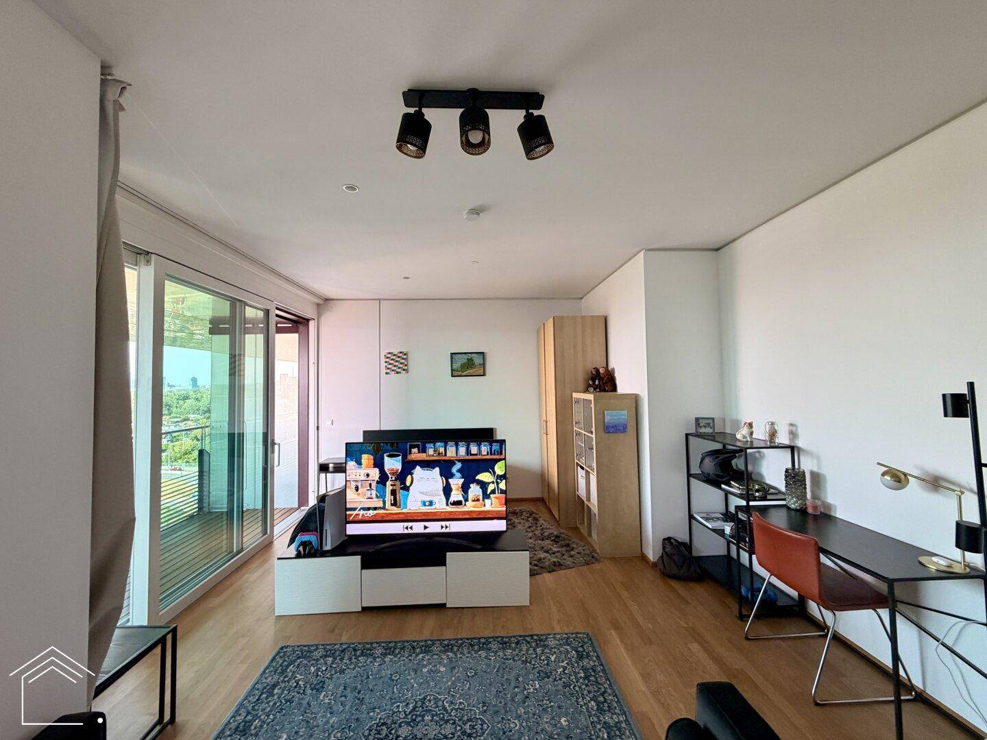 Heller Wohnbereich mit Fernseher, Schreibtisch und Regalen, ausgestattet mit modernen Möbeln.
