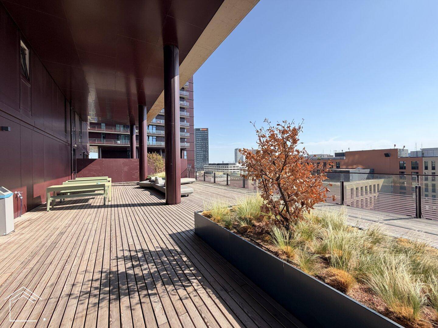 Große Dachterrasse mit Holzbelag, Pflanzenbeeten und Sitzbänken, bietet weite Aussicht.