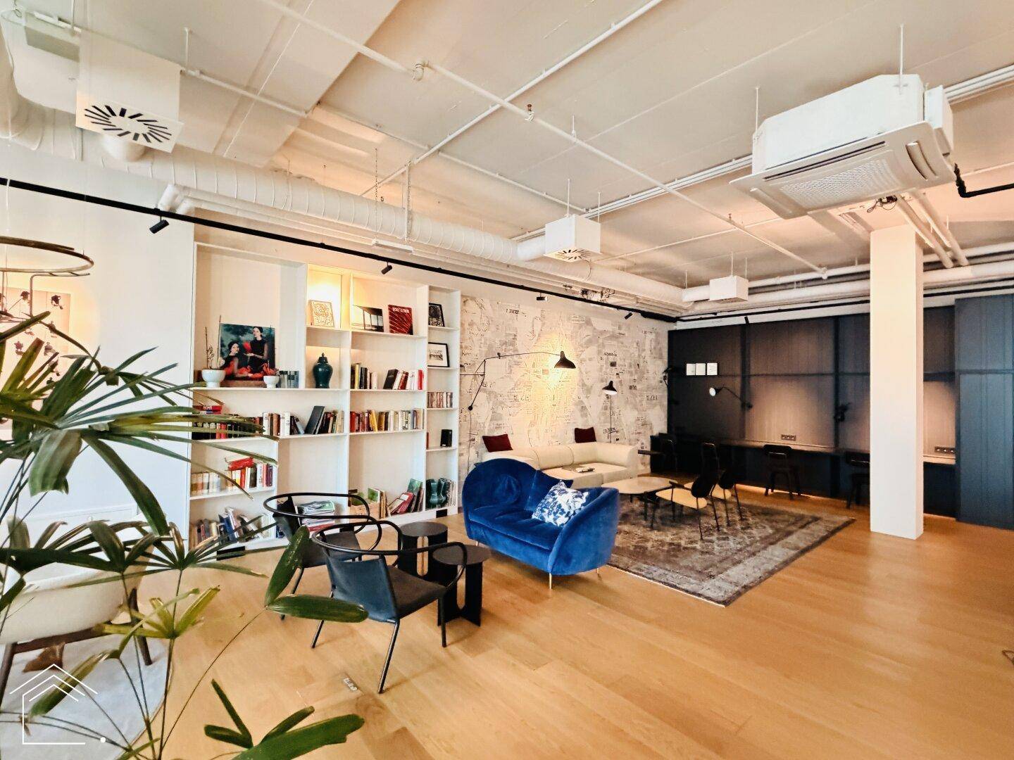 Geräumiger Gemeinschafts-Wohnbereich mit Bücherregalen, Sofa und Pflanzen, industrieller Stil.
