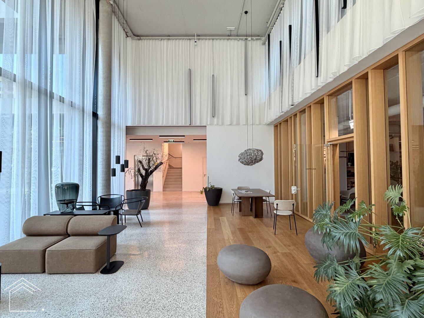 Modernes, lichtdurchflutetes Foyer mit hohen Decken, bequemen Sitzgelegenheiten und Holzvertäfelungen.