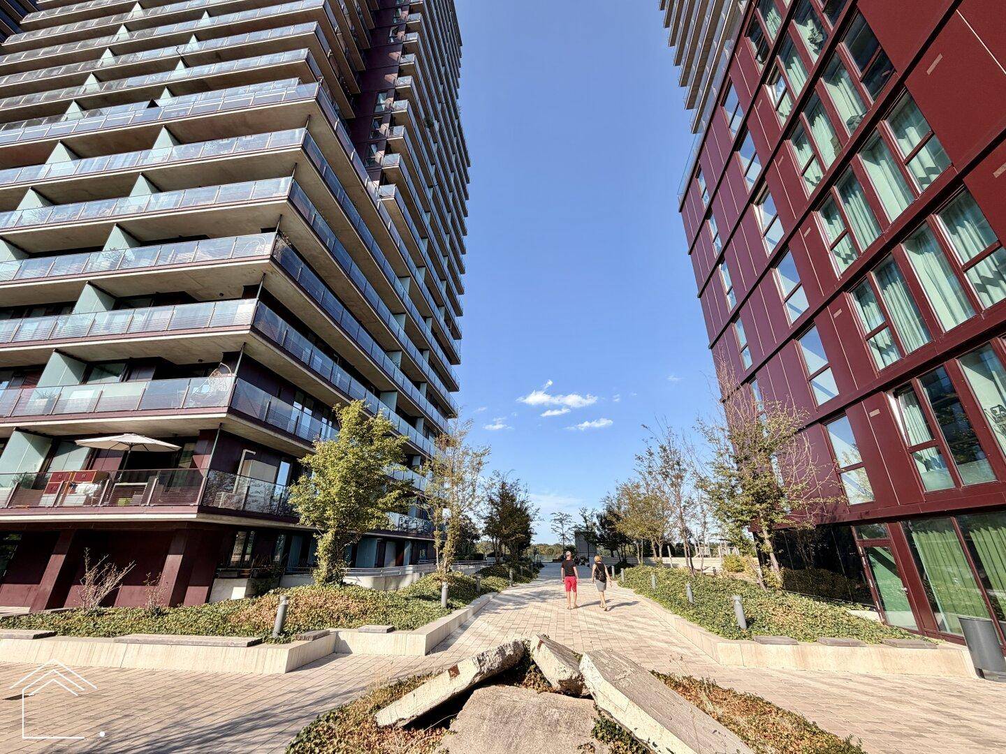 Moderne Hochhäuser mit vielen Balkonen und einer gepflegten Außenanlage unter blauem Himmel.