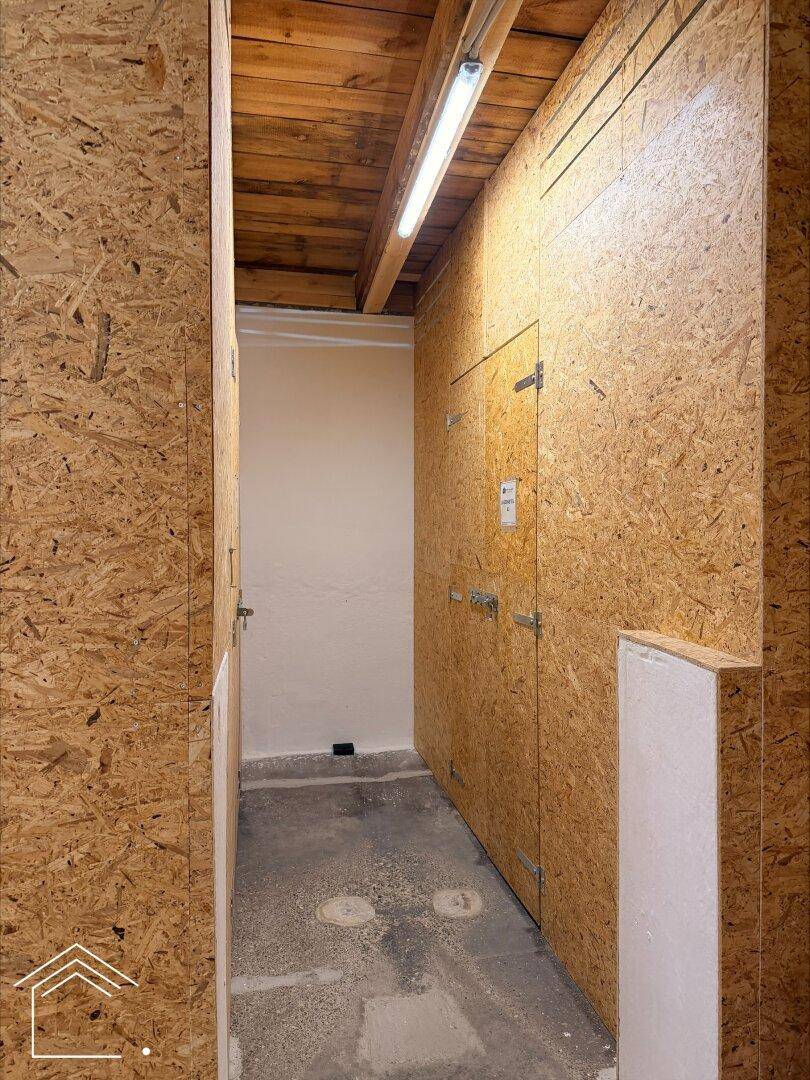 Schmaler Flur mit Wänden aus OSB-Platten, Holzdecke und mehreren Lagertüren.