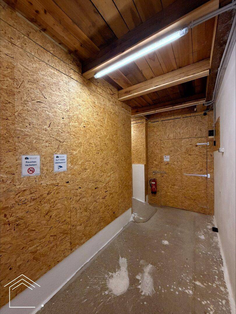 Langer Flur mit OSB-Wänden, Holzdecke, Betonboden und einem Feuerlöscher.