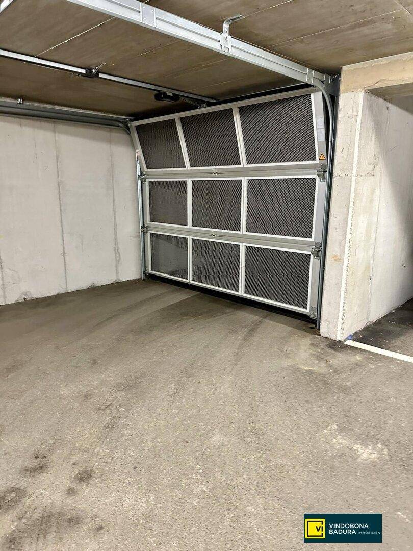 Einzelner Garagenstellplatz in einer Tiefgarage mit geöffnetem Sektionaltor und Betonwänden.